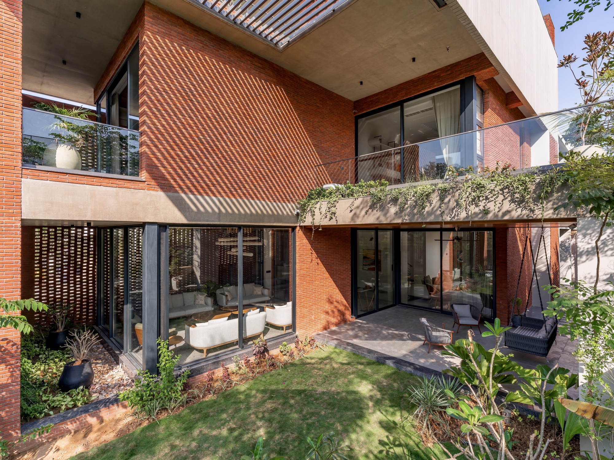 Rear courtyard with glass walls, planted balconies, and brick screens casting shadow patterns