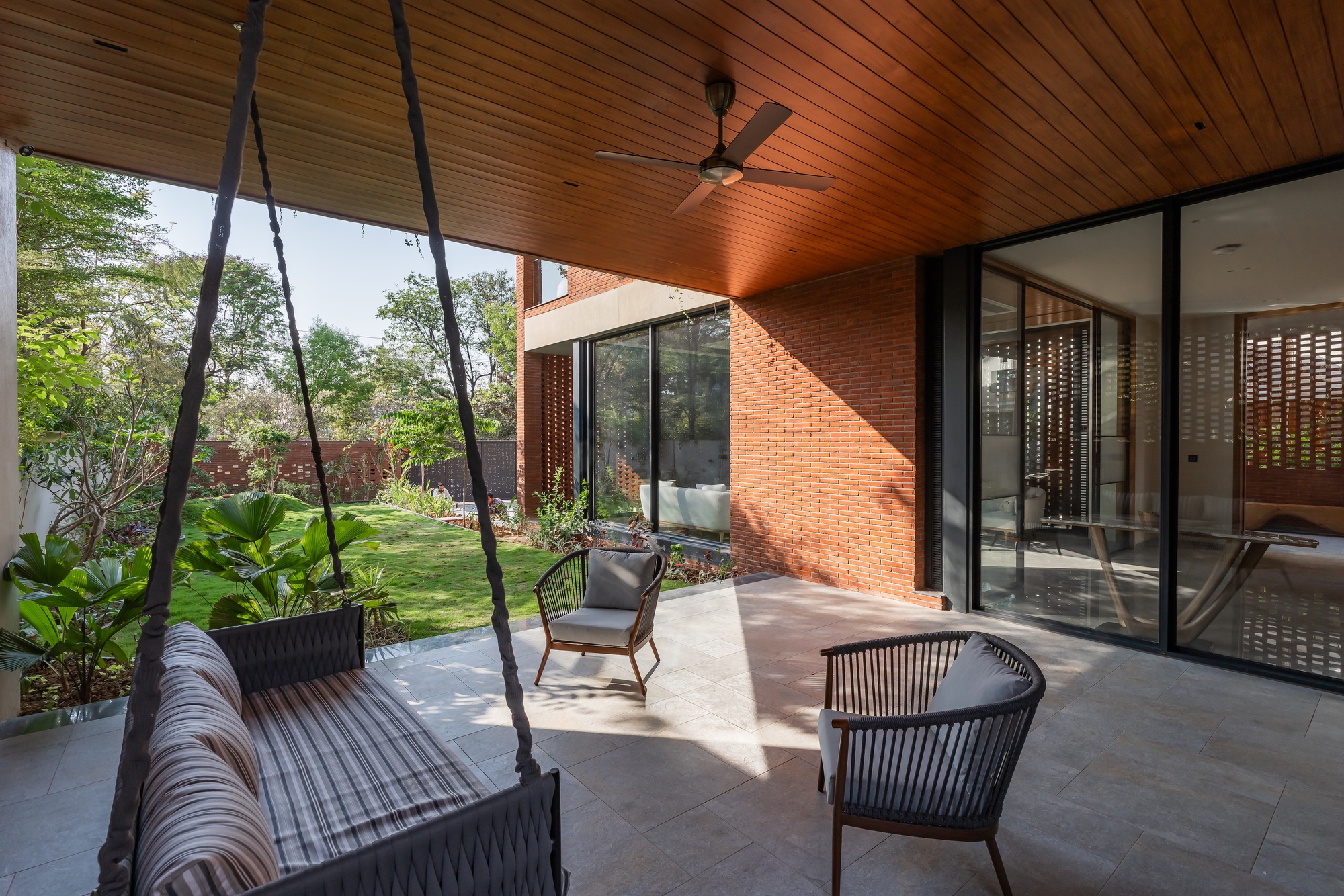 Shaded terrace with suspended rope swing and timber ceiling overlooking a landscaped garden