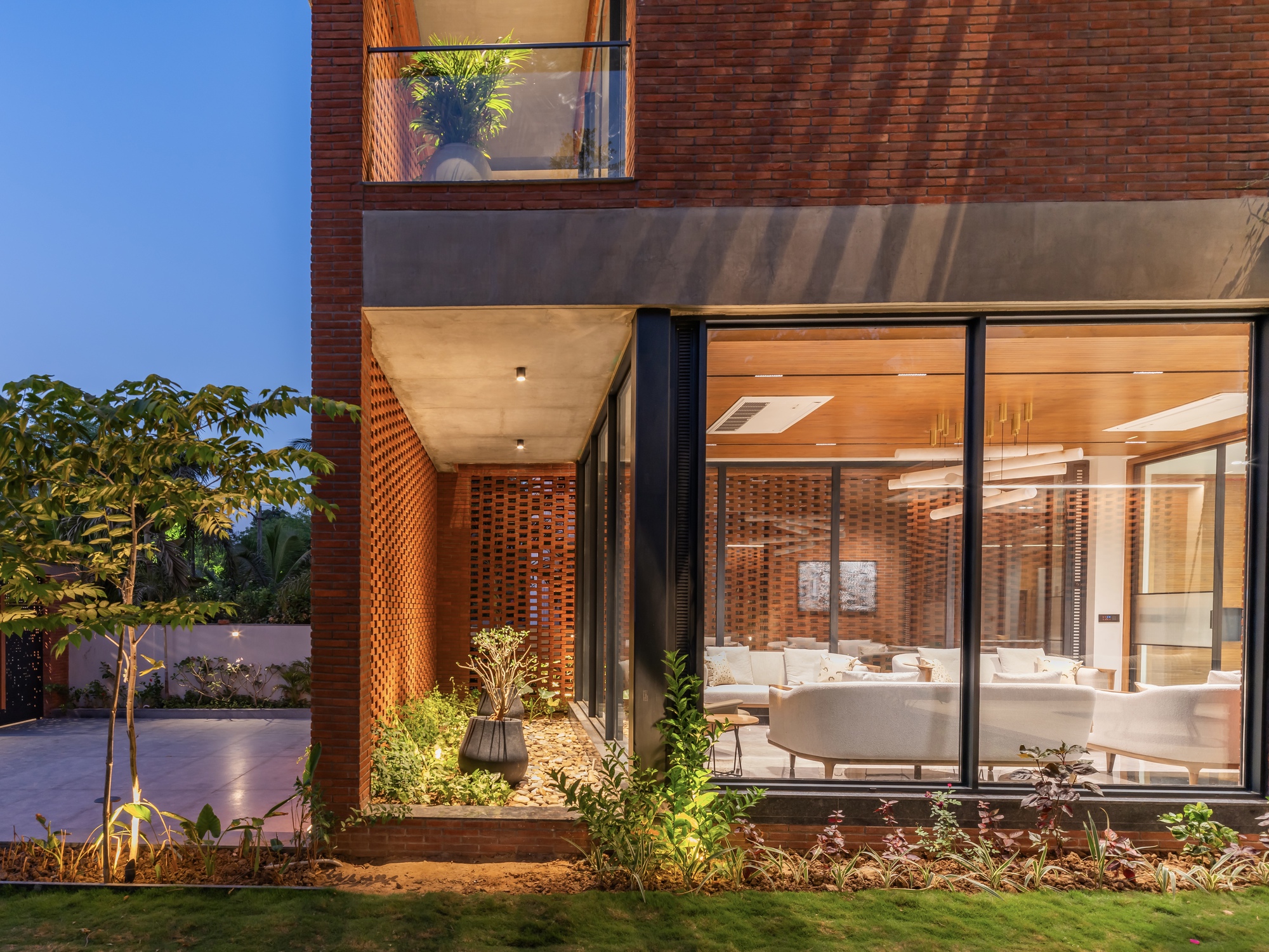 Exterior corner illuminated at dusk showing perforated brick entry and full-height glazing with interior lights