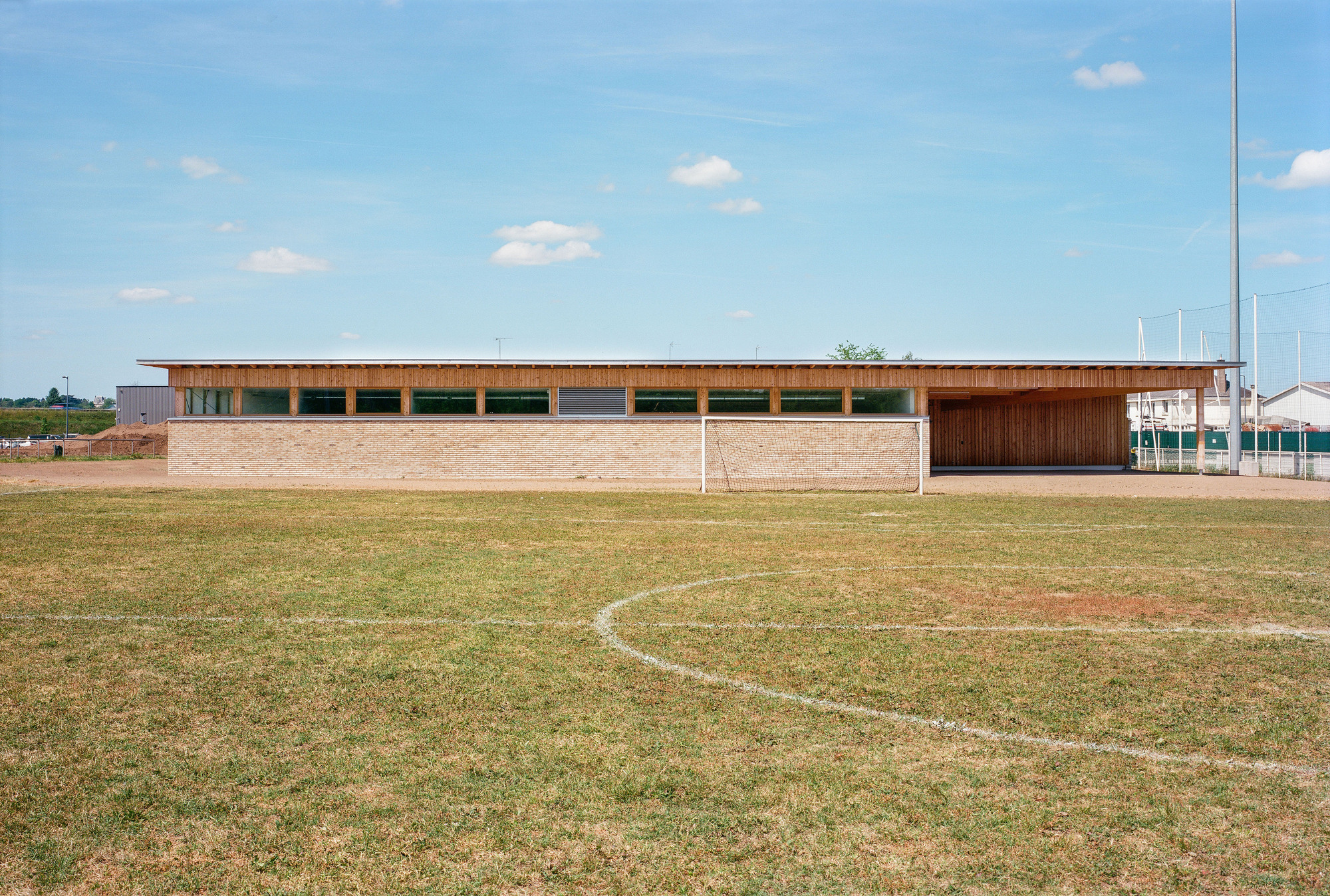 Long facade with horizontal timber clerestory above a pale brick base facing the sports field