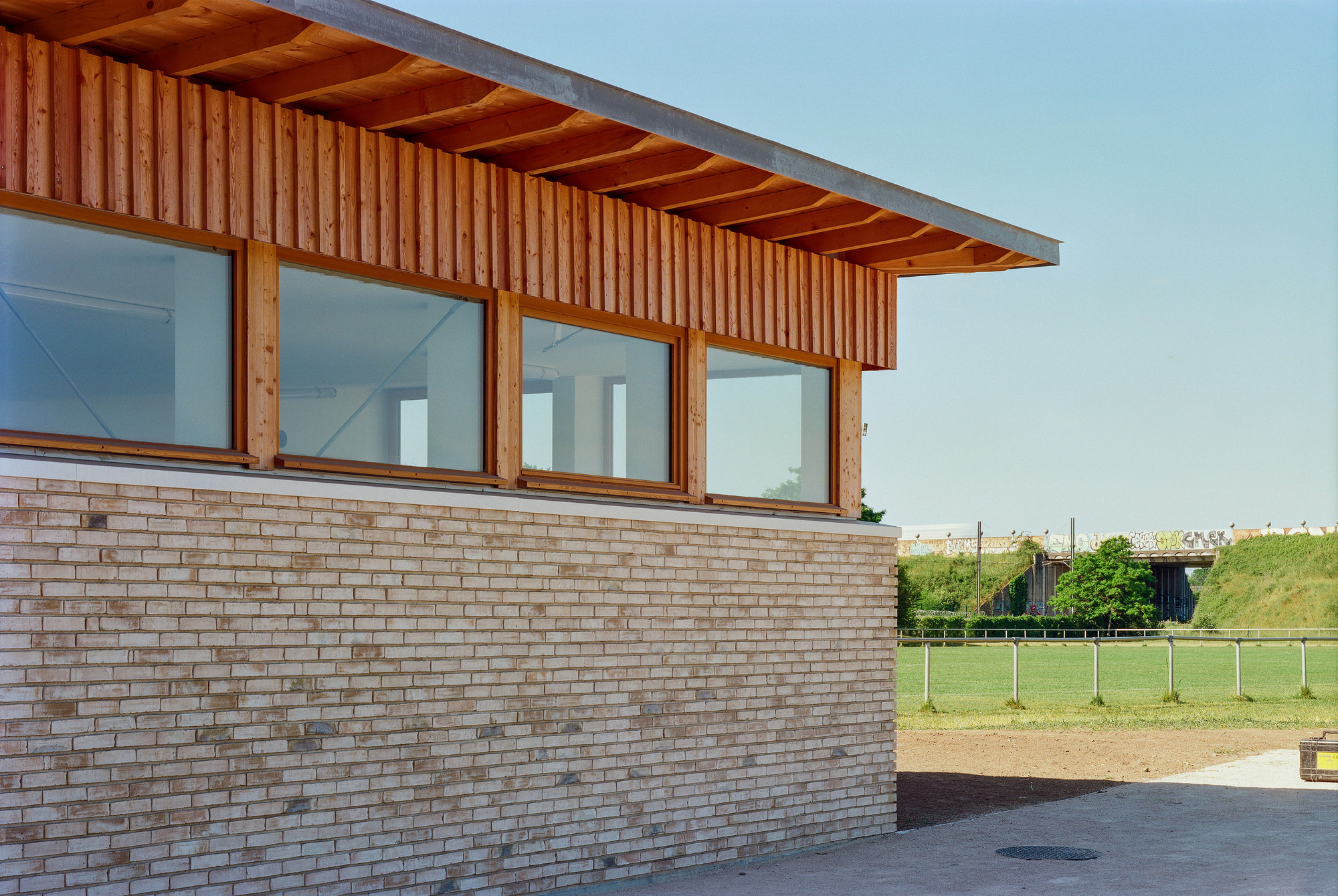 Corner detail showing vertical timber cladding above tan brick with glazed openings under overhanging eaves