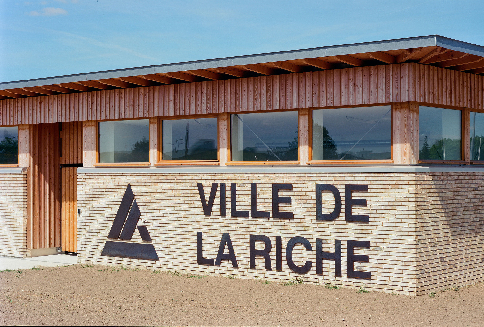 Entrance facade with horizontal timber cladding and large signage applied to the wood siding in the afternoon
