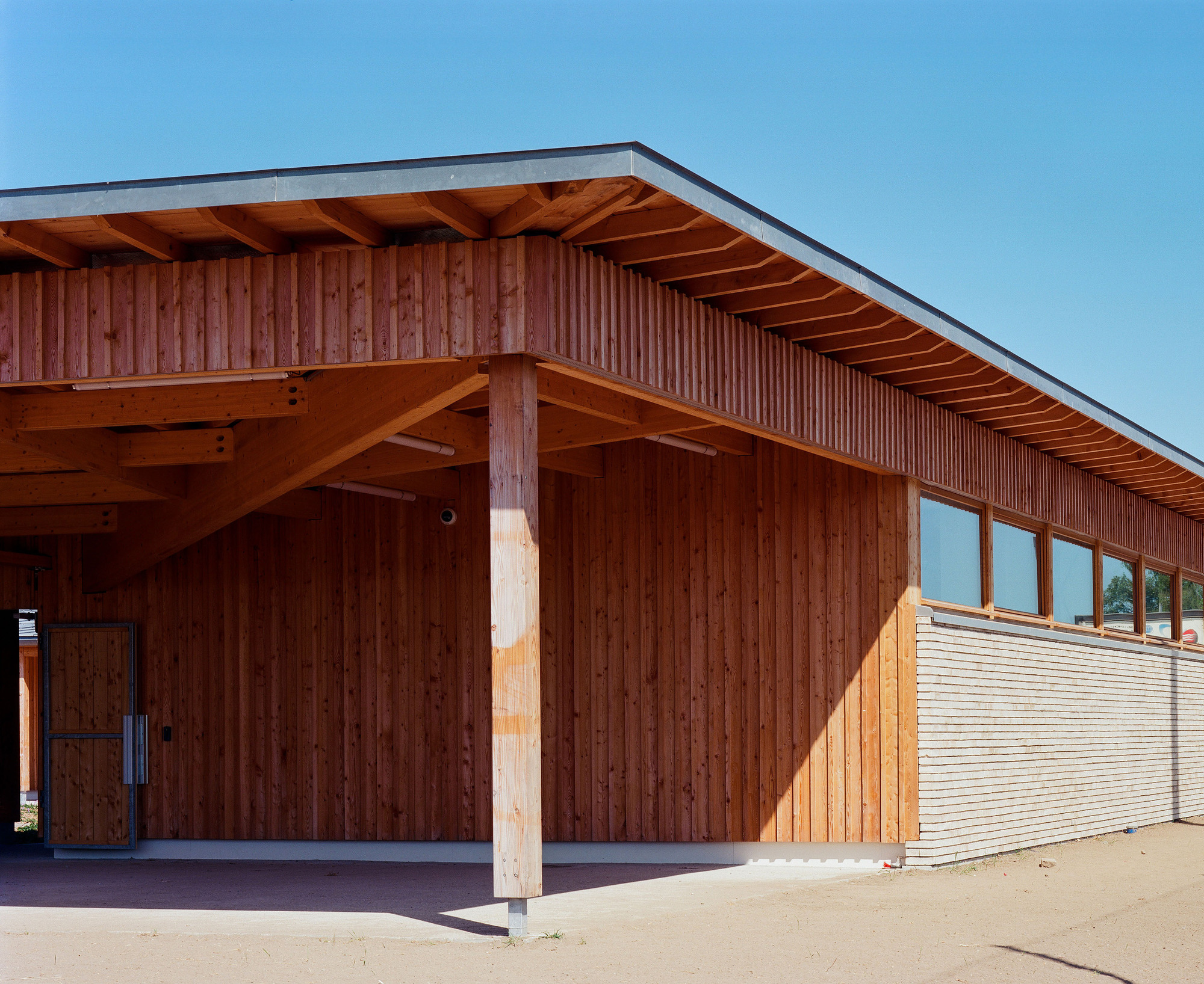 Corner view of timber-clad pavilion with exposed rafters and an open covered area beneath the cantilevered roof