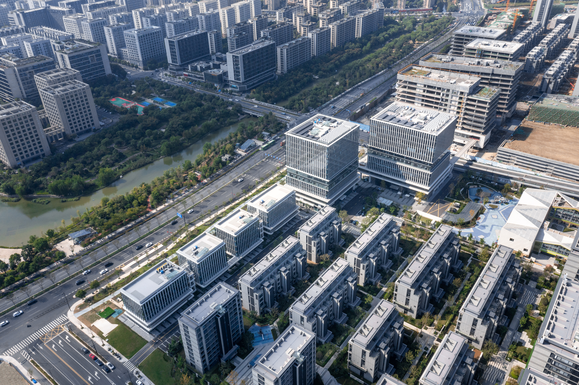 Aerial view of mixed-use development with striped facade towers and low-rise residential blocks beside a river