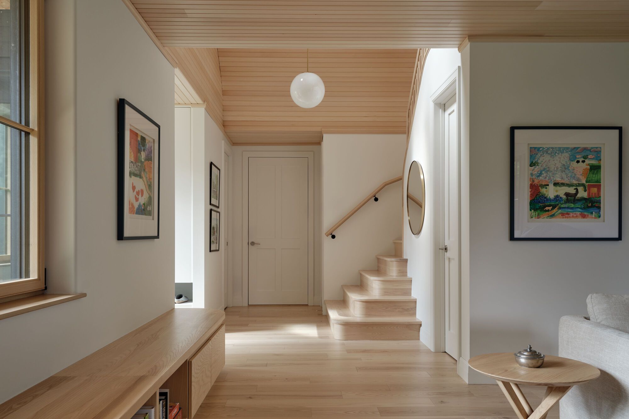 Interior hallway with wood-clad ceiling, pale timber stair and globe pendant casting sunlight across the floor