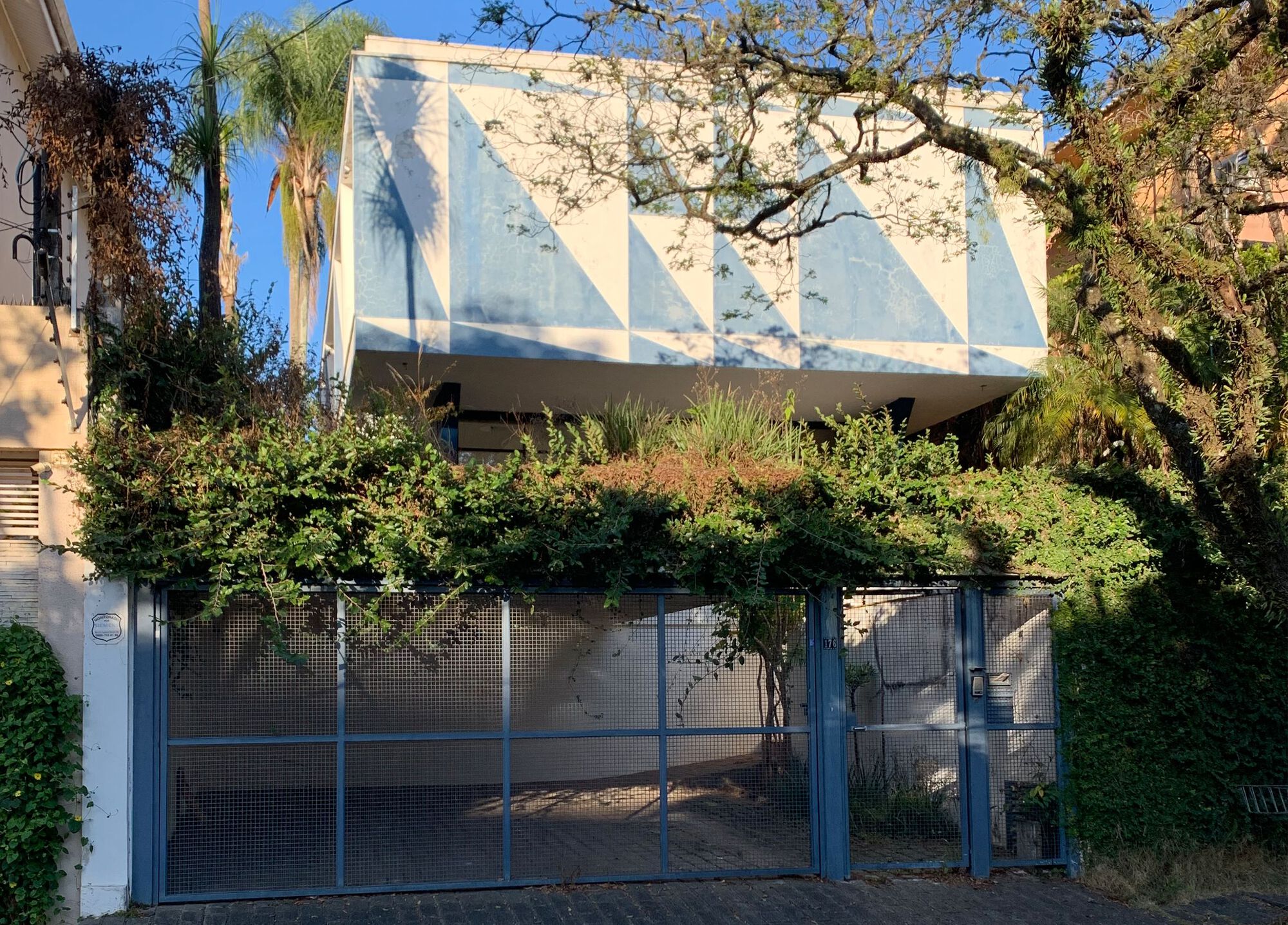 View from street showing cantilevered volume with geometric facade behind mesh gate and bare tree