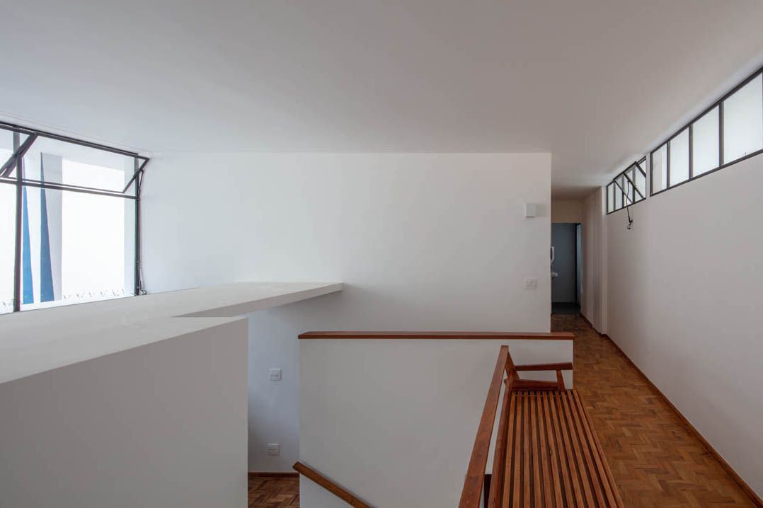 Upper level hallway with wooden railing overlooking stairwell and white walls lit by clerestory windows