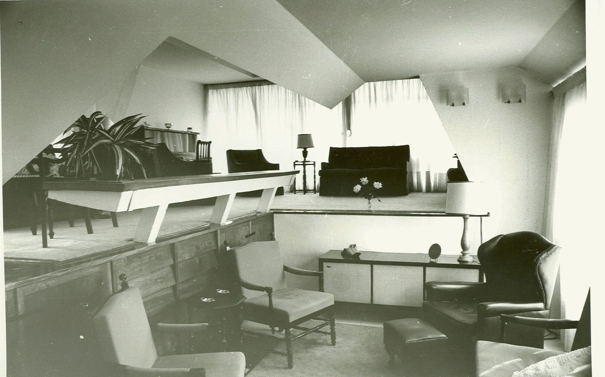 Split-level interior with angular ceiling planes, mid-century furniture and potted plants in diffused natural light