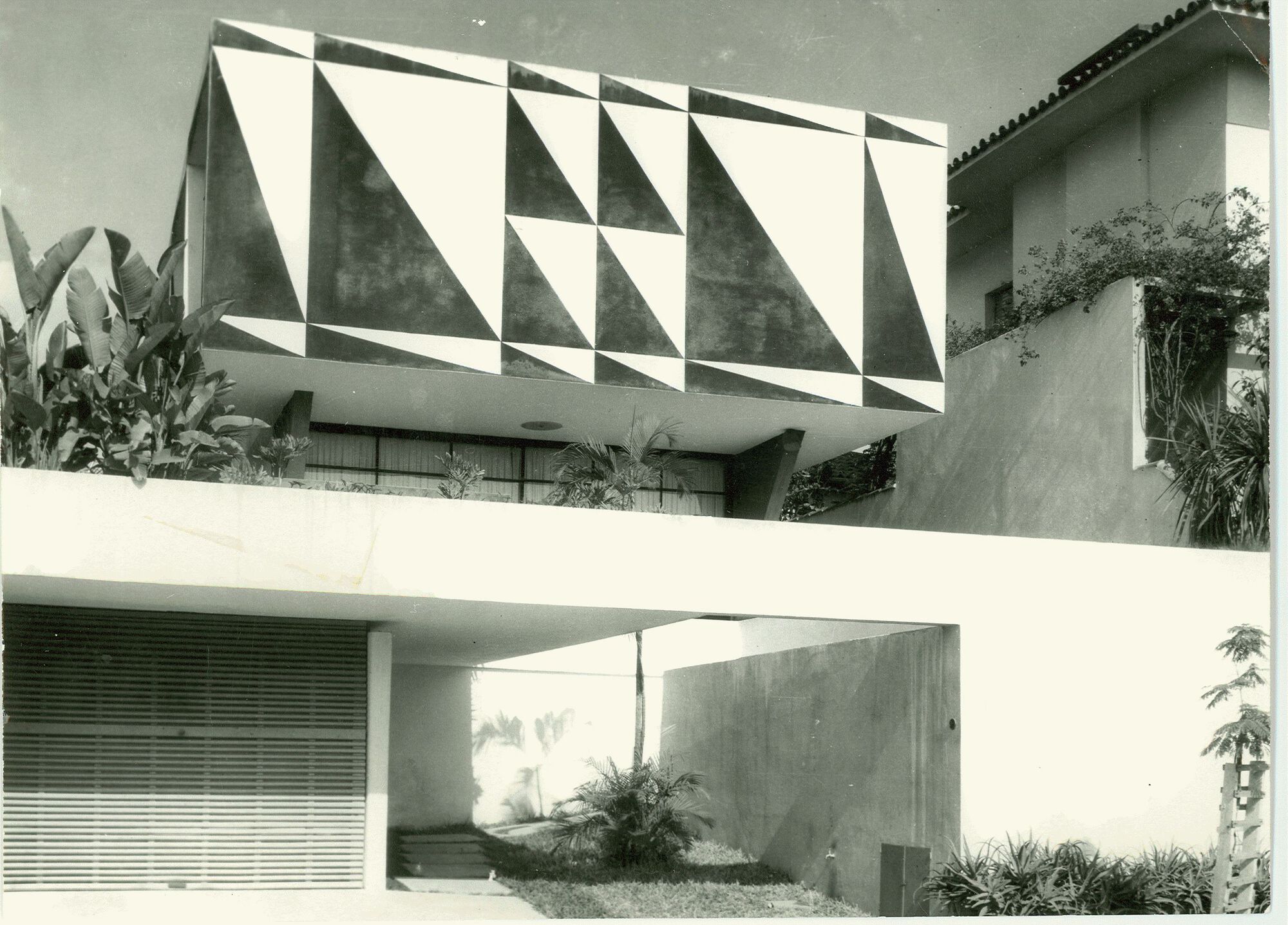 Upper volume with geometric triangular facade panels above a recessed entry courtyard with planted beds