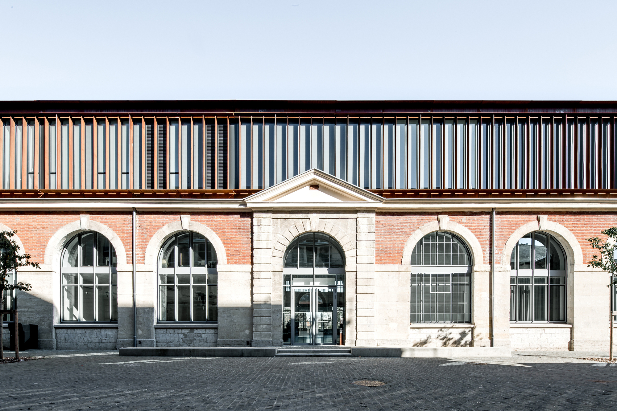 Street facade with arched windows in brick and stone below a vertical slatted timber upper storey