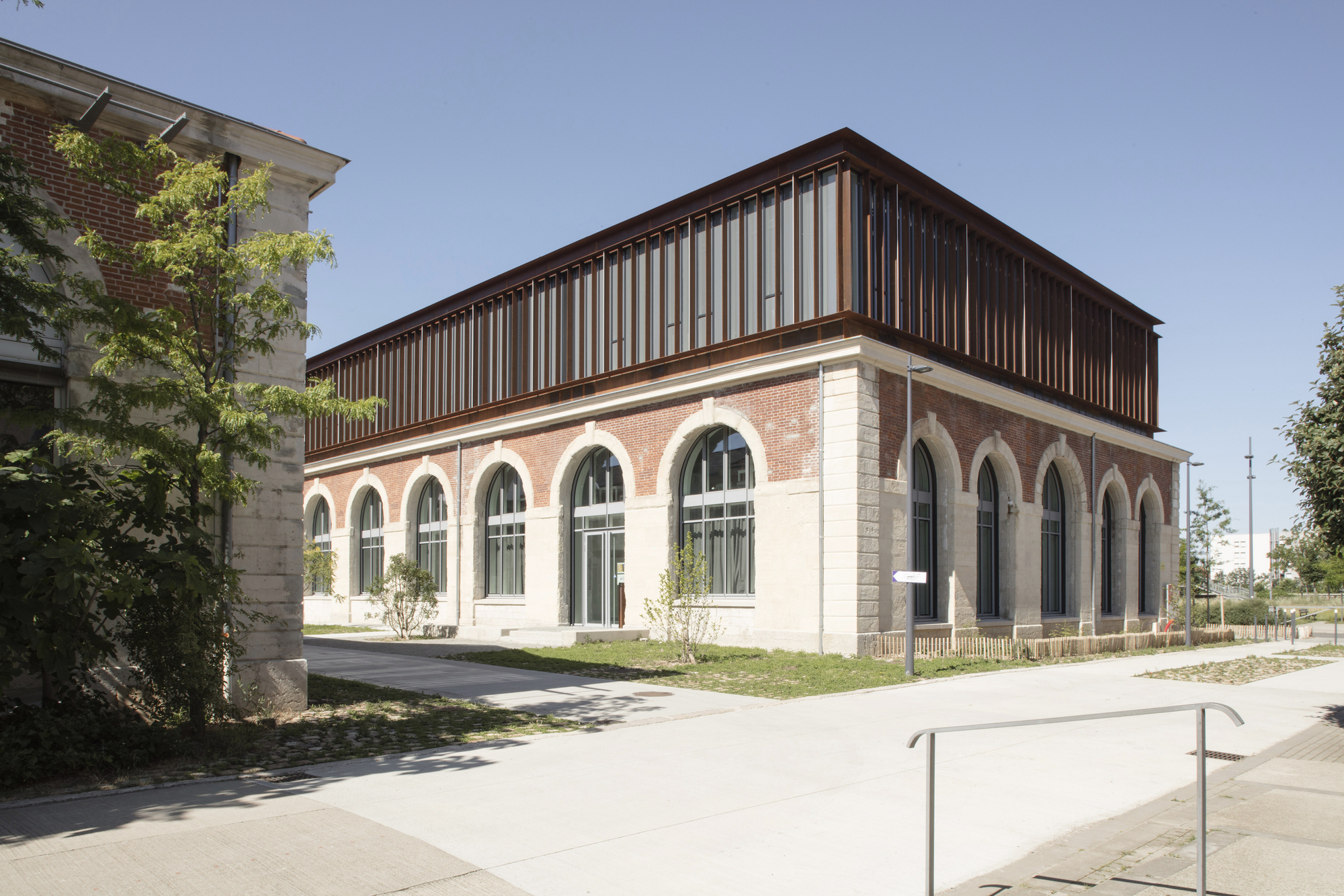 Corner view of the restored masonry volume with timber-slatted addition above arched window bays
