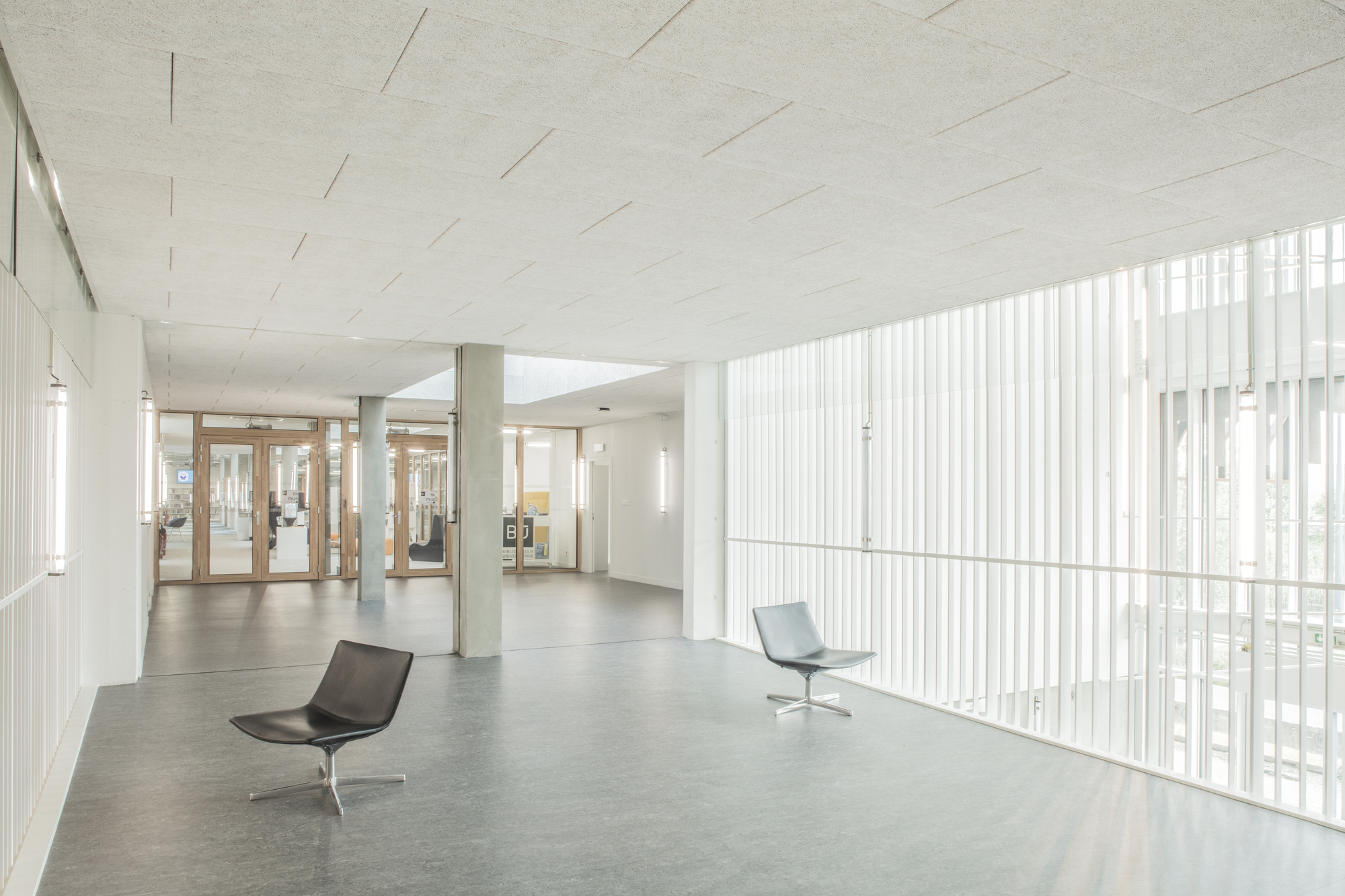 Interior lobby with vertical white screen walls, polished concrete floor and two lounge chairs