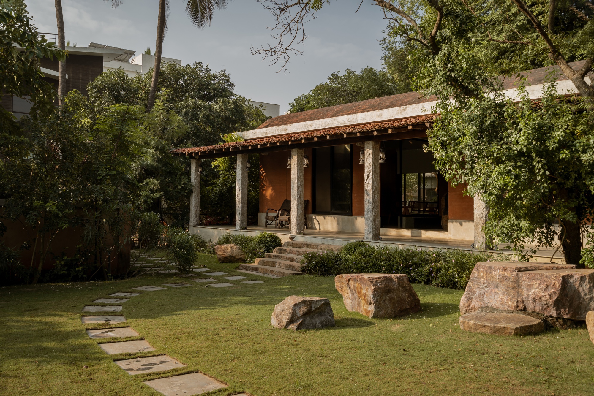 Open veranda with rough stone columns and ochre walls facing a lawn with large rock formations