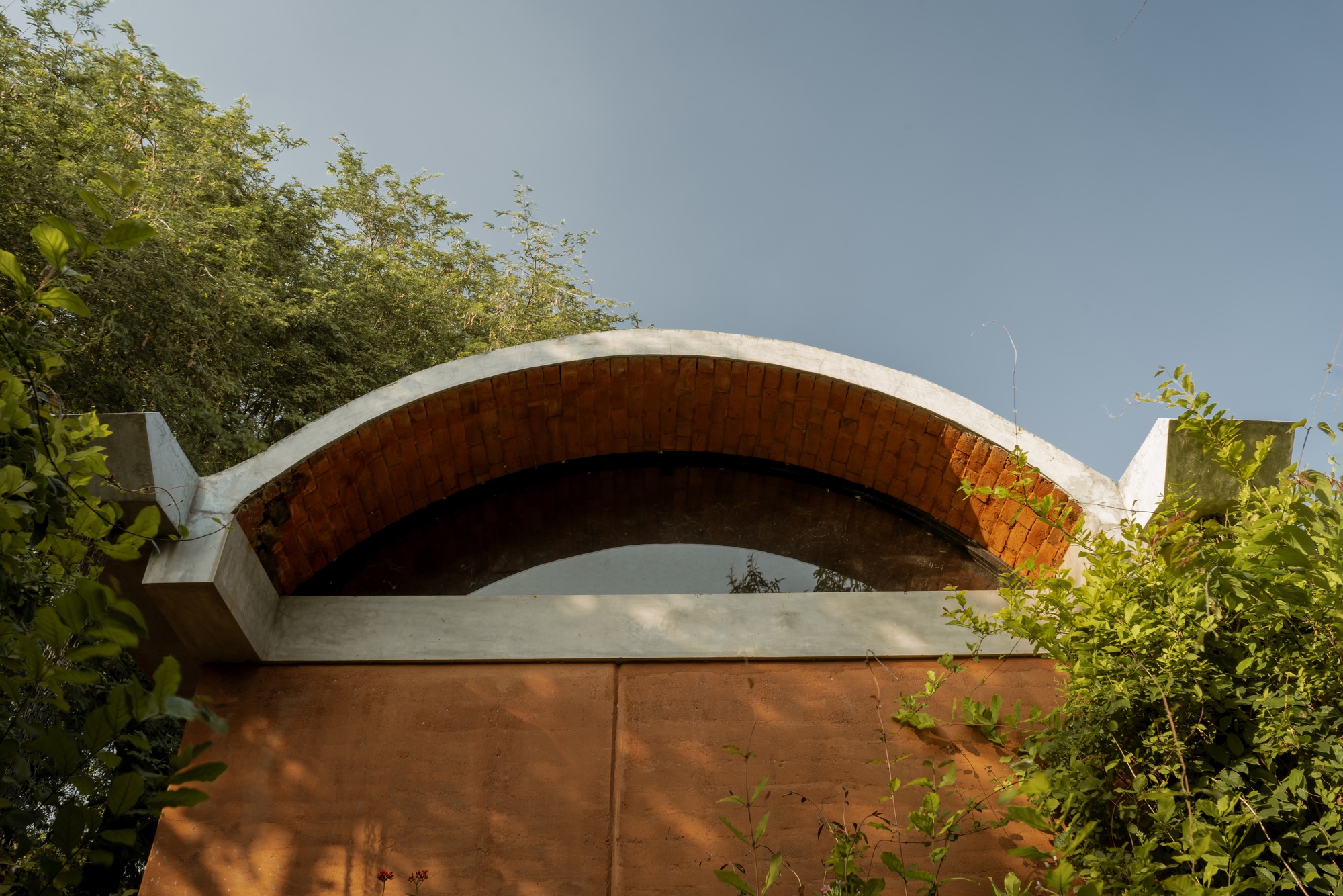 Exterior view of the exposed brick vault with concrete edge beam framed by foliage