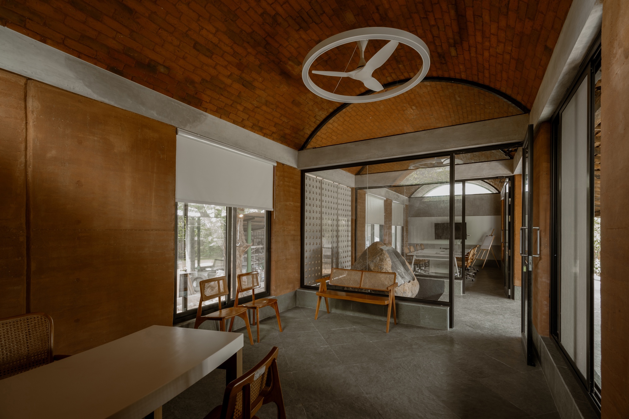 Interior living space with woven timber ceiling vault and glass doors opening to a courtyard with sculpture