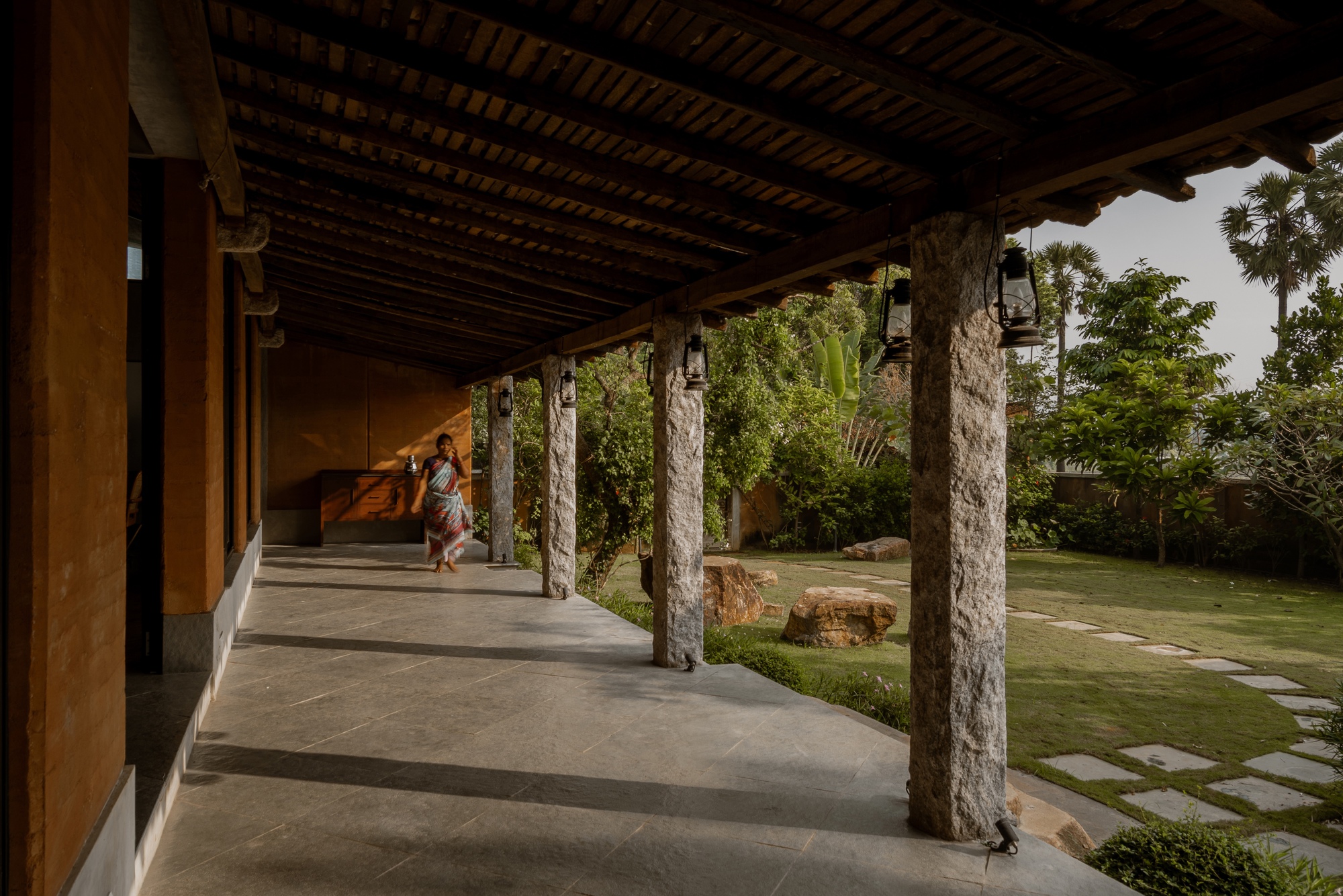 Covered veranda with exposed timber ceiling and cylindrical stone columns overlooking a garden lawn