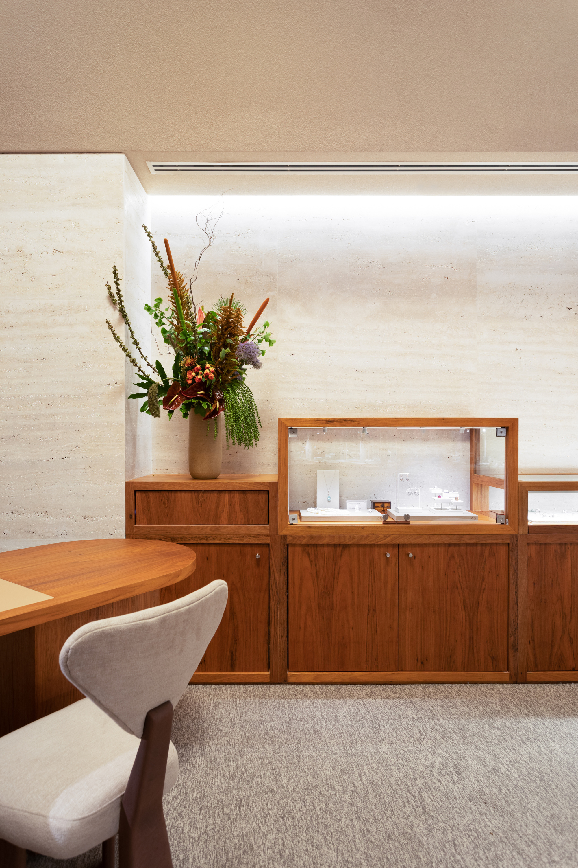 Walnut credenza and glass vitrine below a horizontal window with floral arrangement