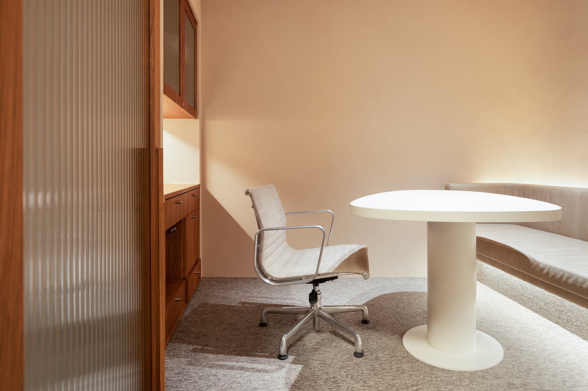 White pedestal table beside timber cabinetry with reeded glass panel under warm ambient light