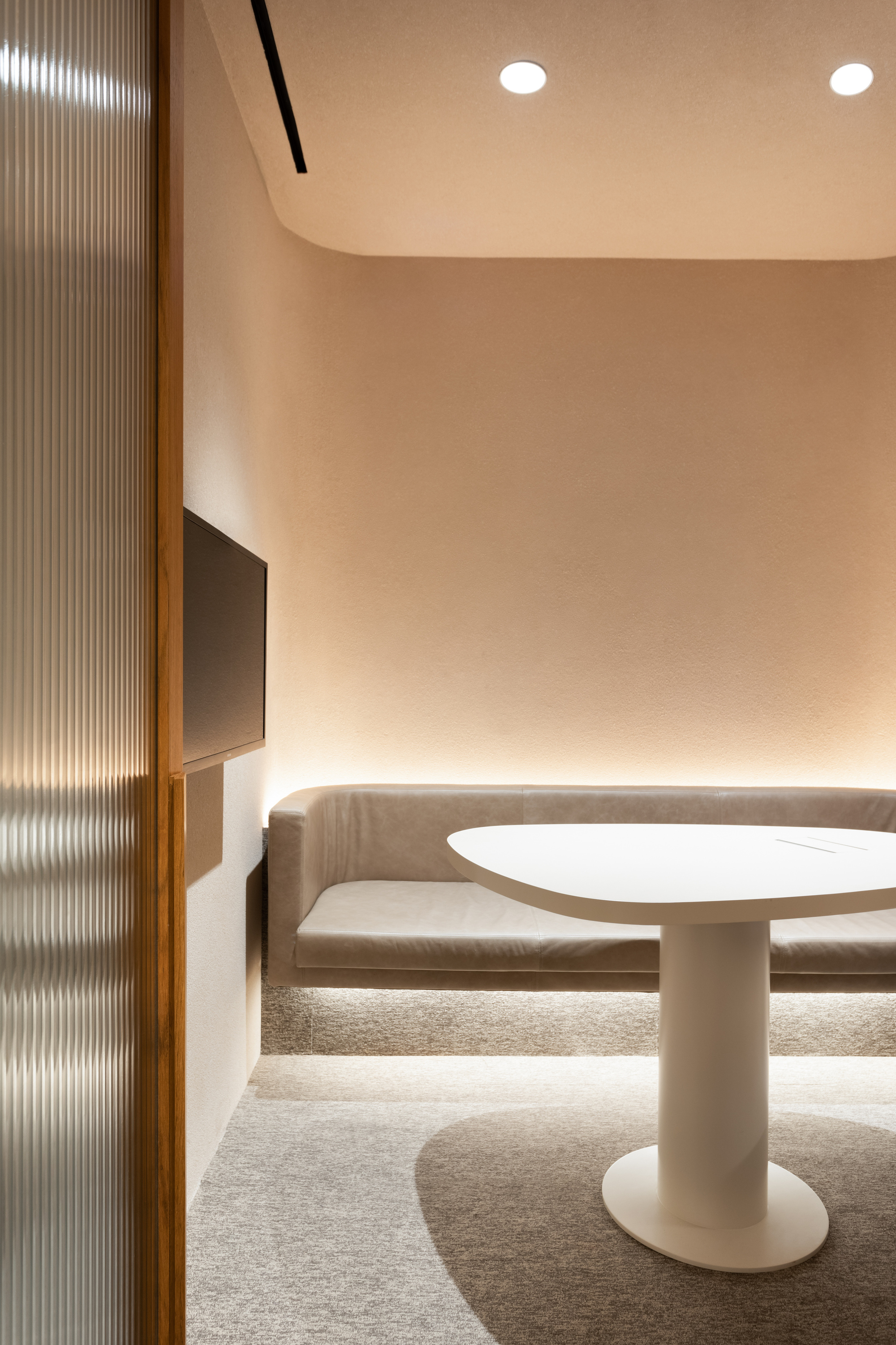 Curved banquette seating around a white pedestal table with ribbed glass partition and recessed lighting