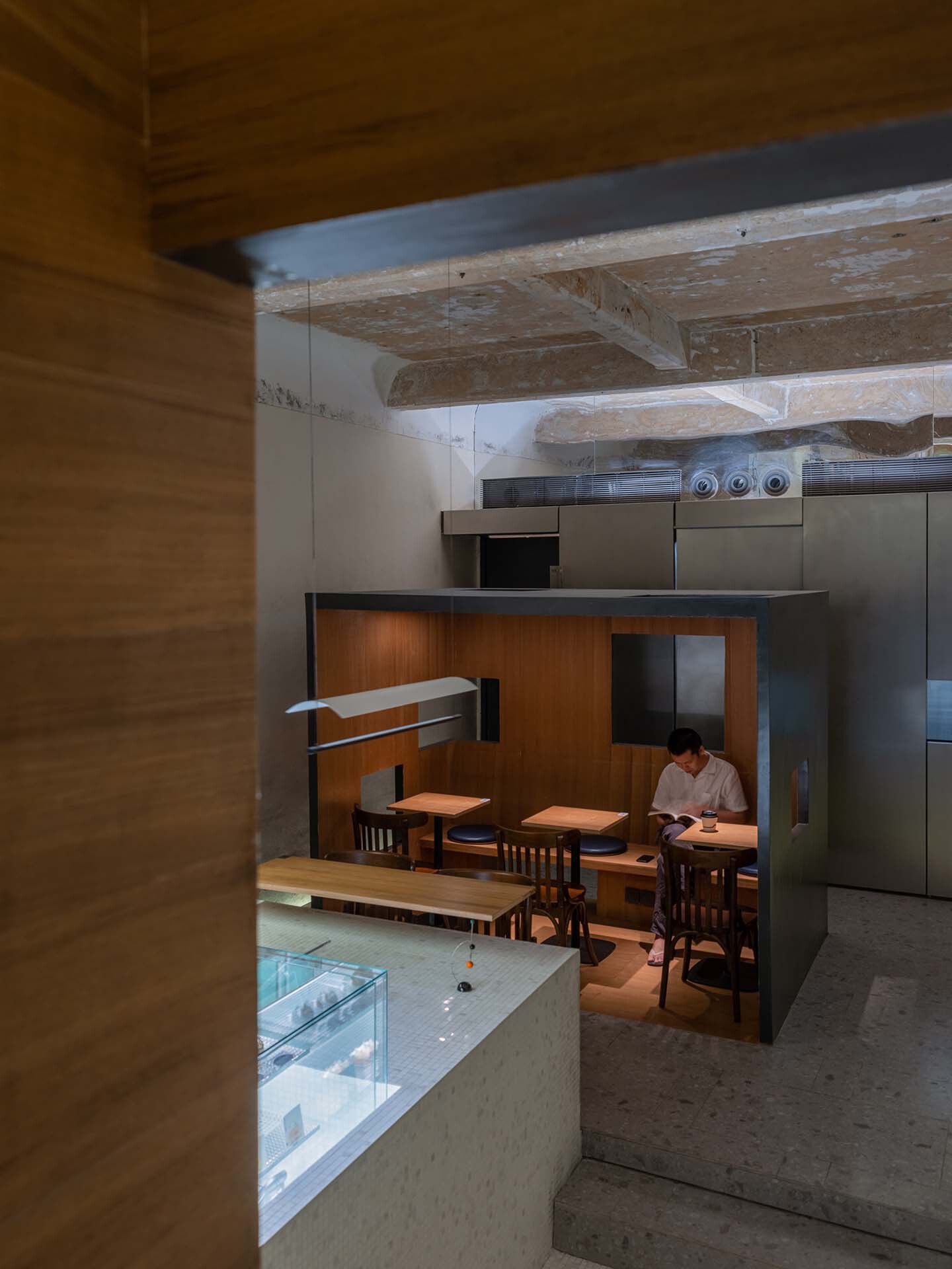 View through timber-clad opening toward dining area beneath exposed timber beams with weathered finish