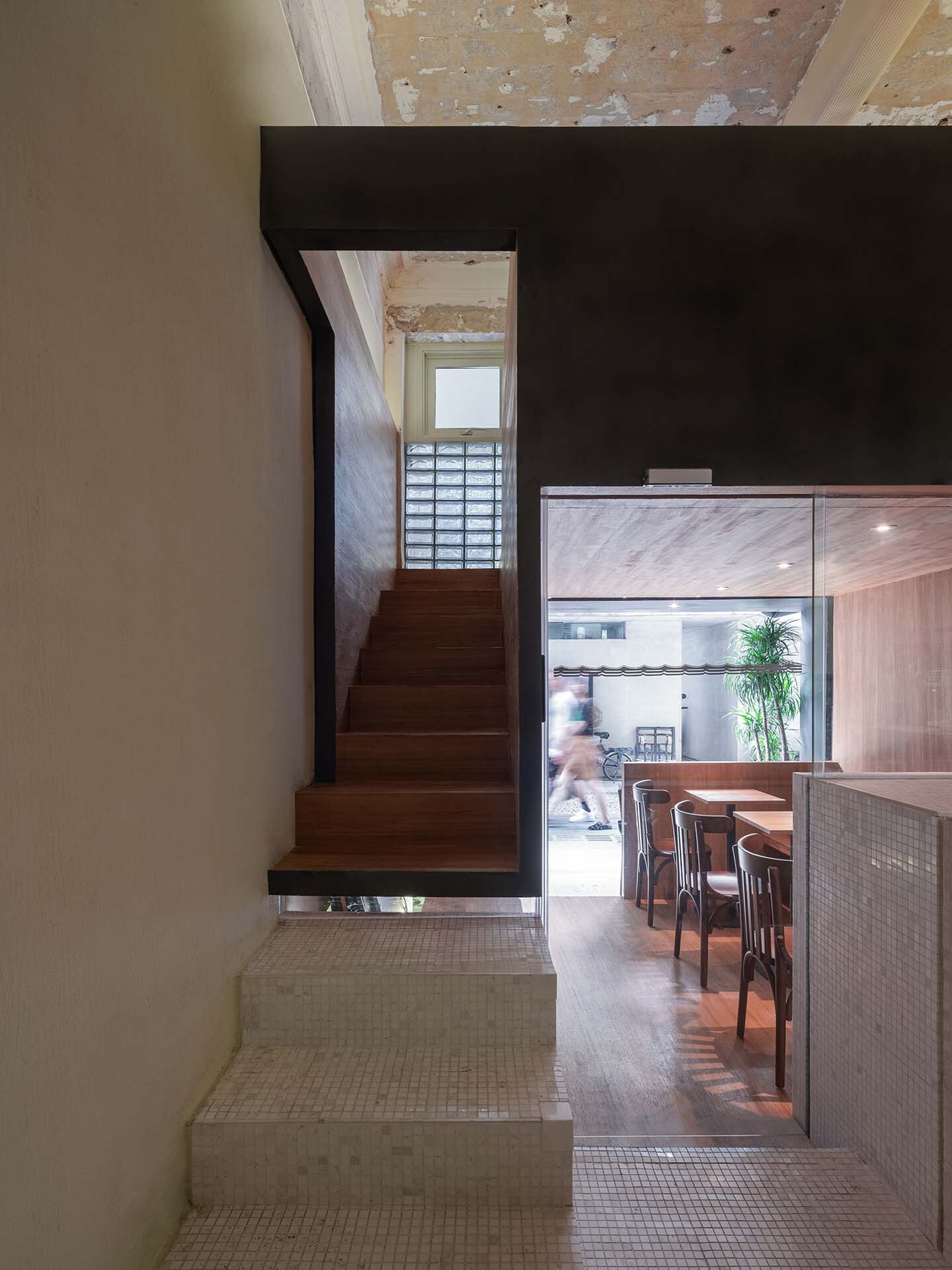 Timber staircase rising within black steel frame opening to glazed block facade above dining area