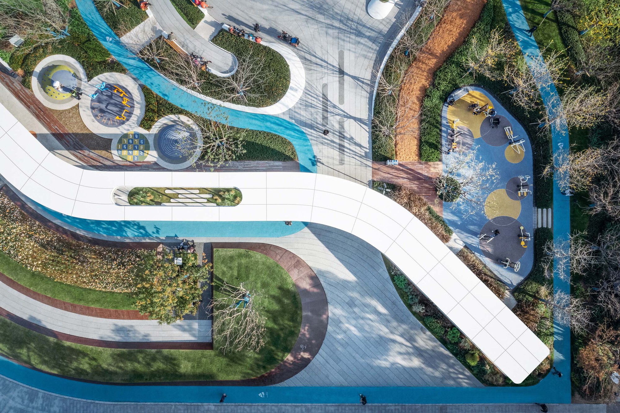 Overhead view showing blue running track weaving around planted zones and play areas