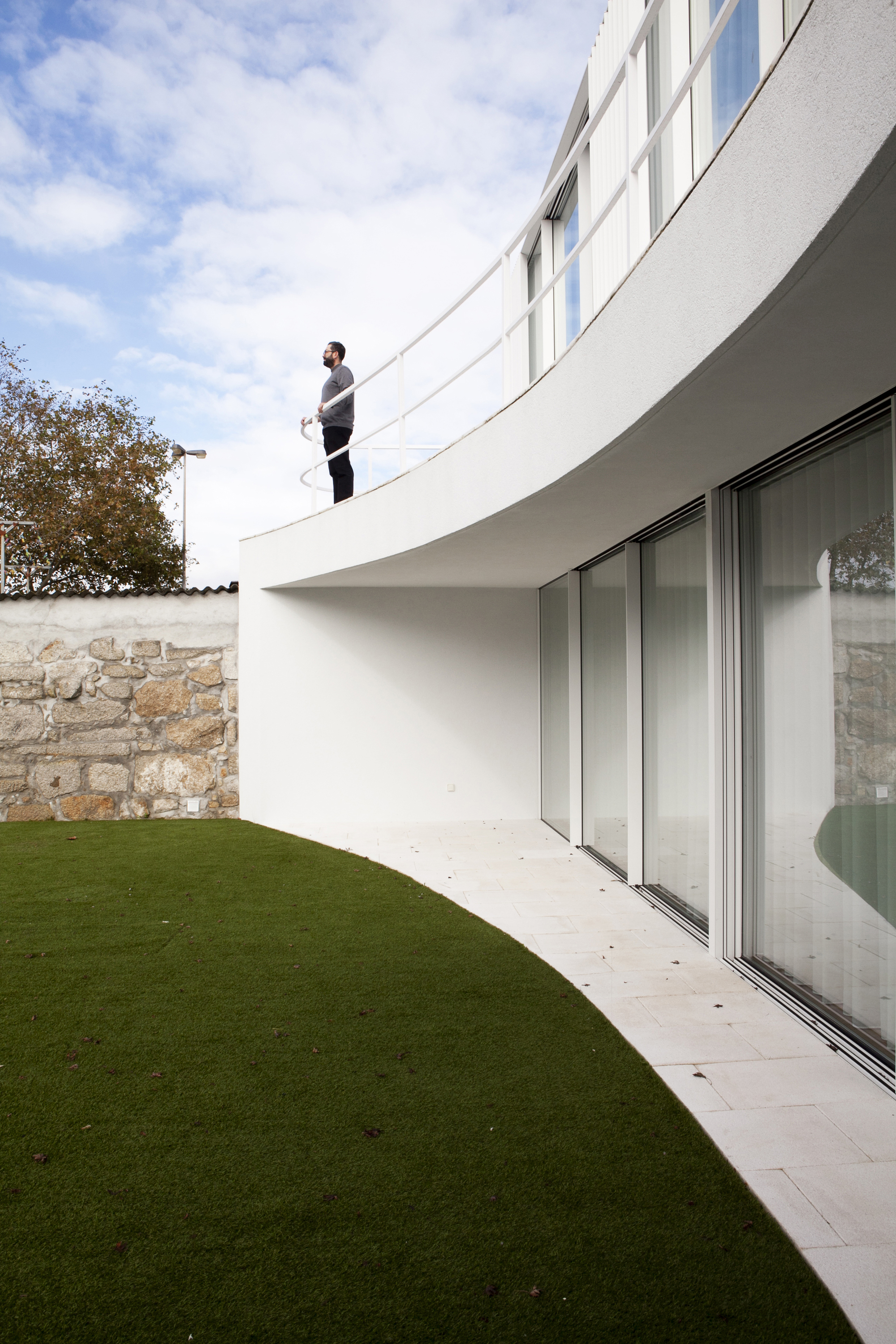 Curved terrace balcony with sliding glass doors overlooking a lawn and stone boundary wall