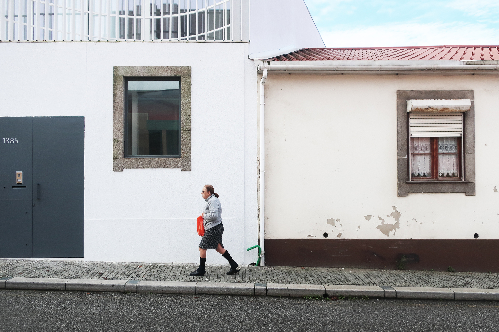 Street view of white rendered facade with granite-framed window and grey door, person walking past