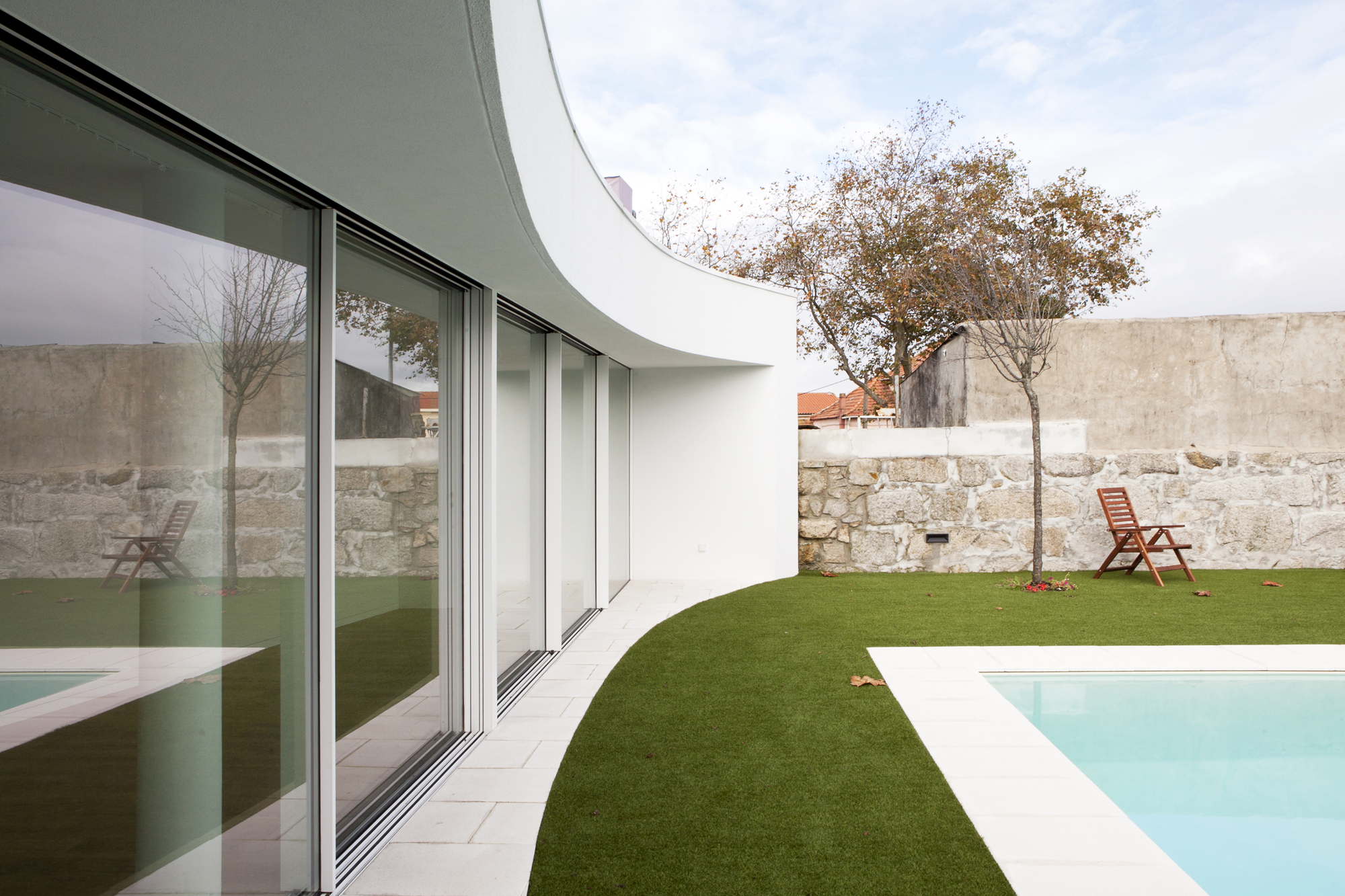 Private courtyard with curved white wall, sliding glass doors, artificial lawn, and pool beside stone wall