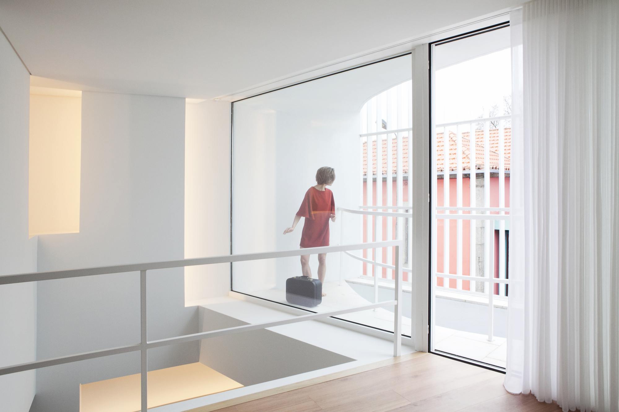 Double-height space with child standing on balcony threshold overlooking street through glass door