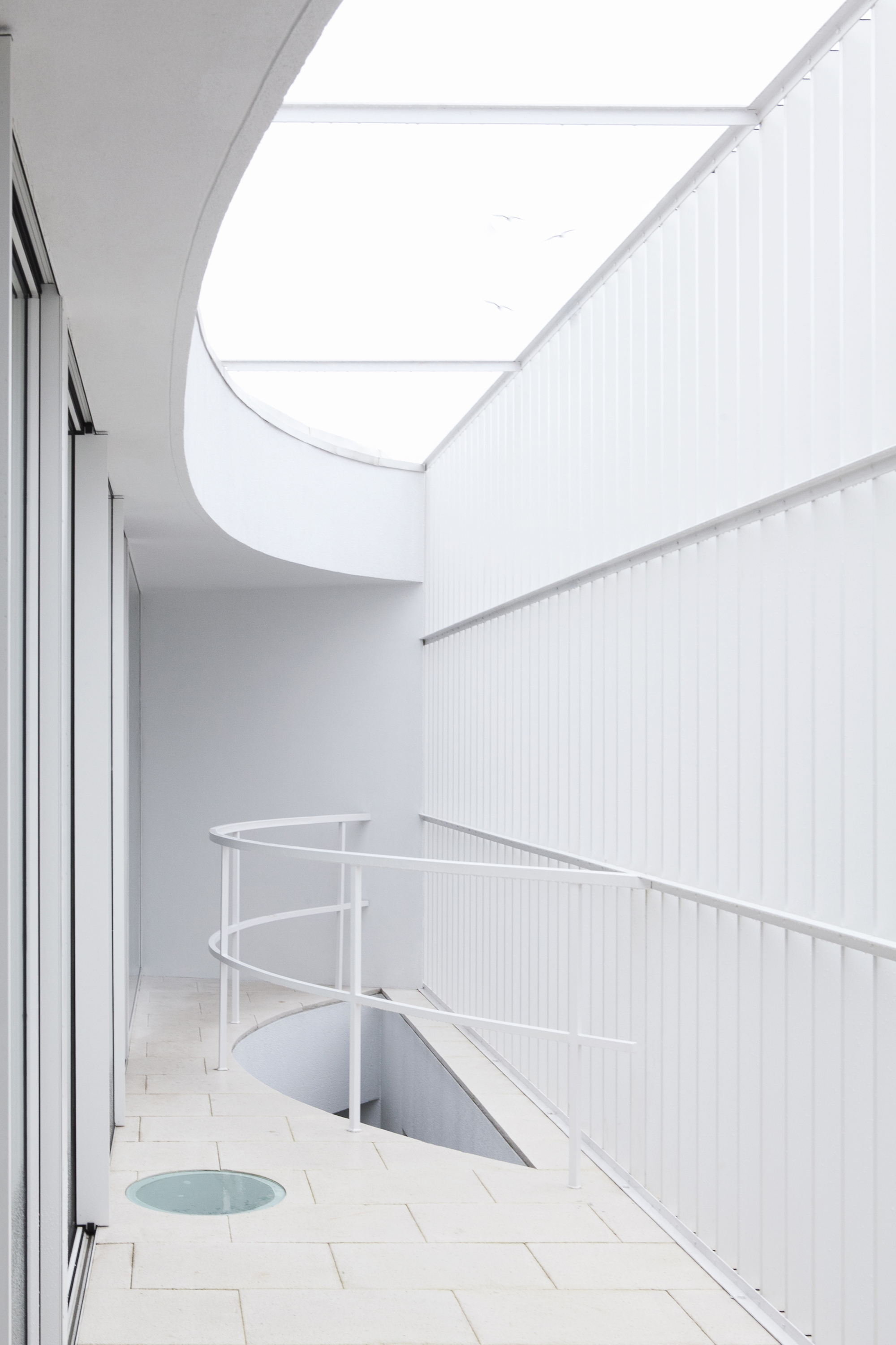 Upper terrace with curved roof overhang, tiled floor, metal balustrade, and skylight opening
