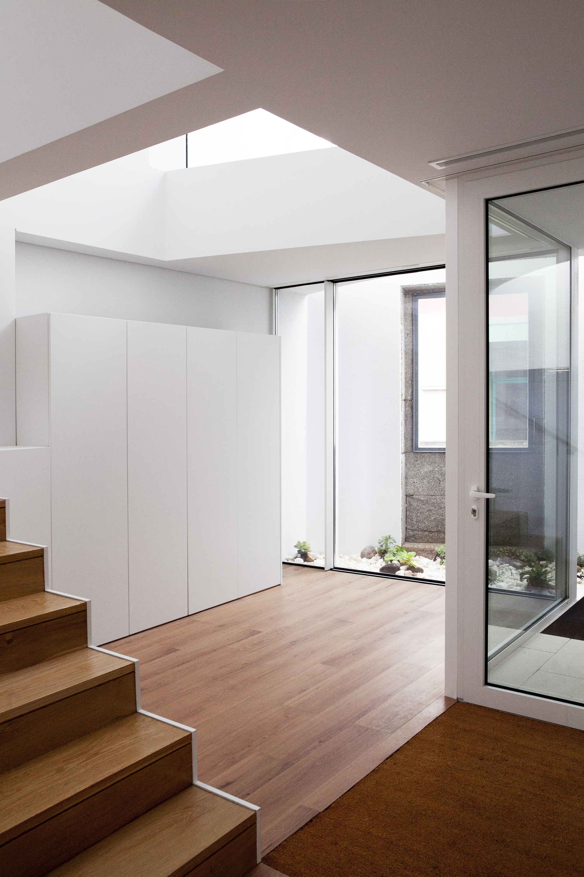 Interior view of timber staircase beside white storage wall with skylight overhead and courtyard window