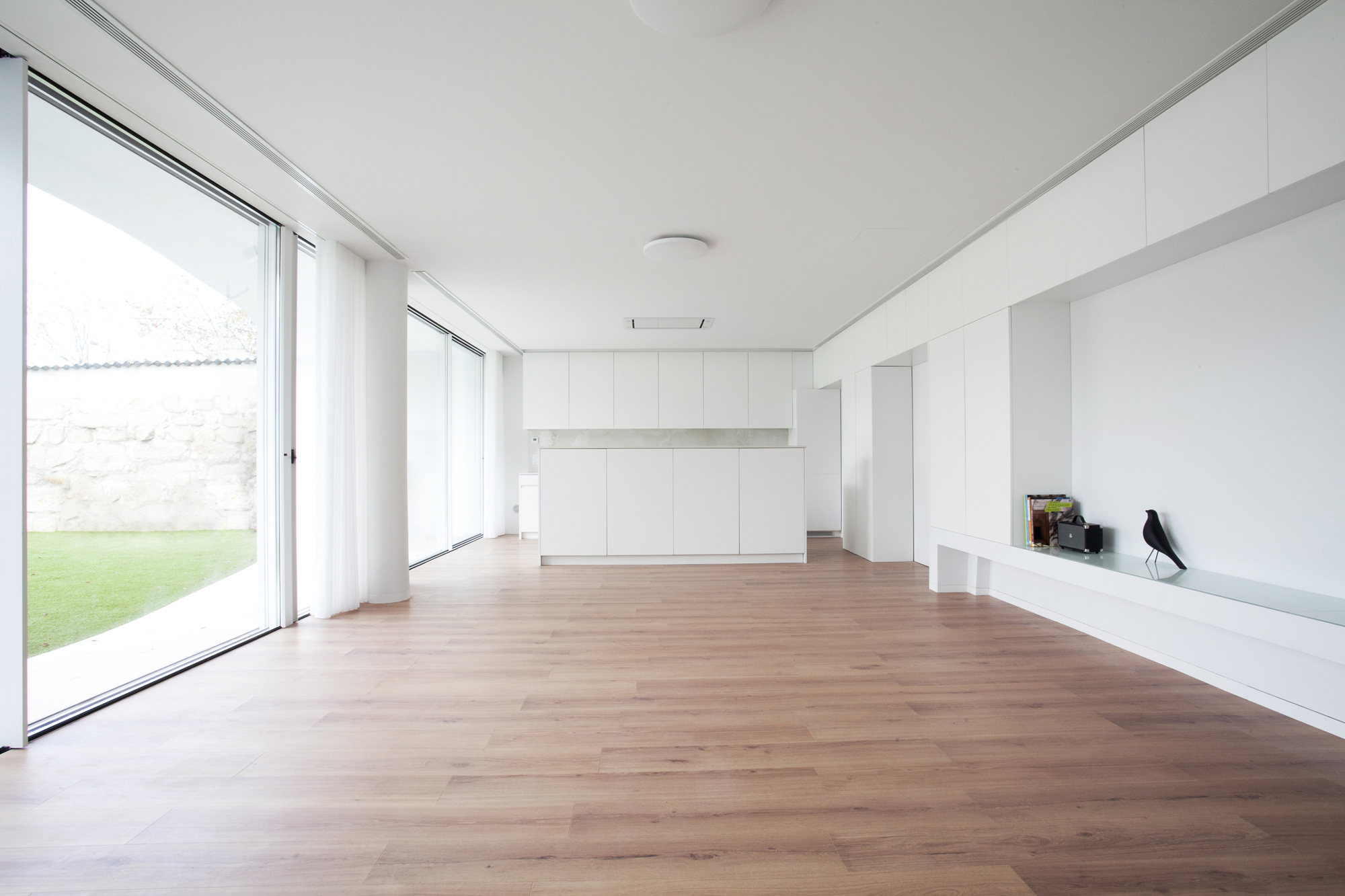 Open living area with timber flooring, white built-in storage, and glazed doors to lawn