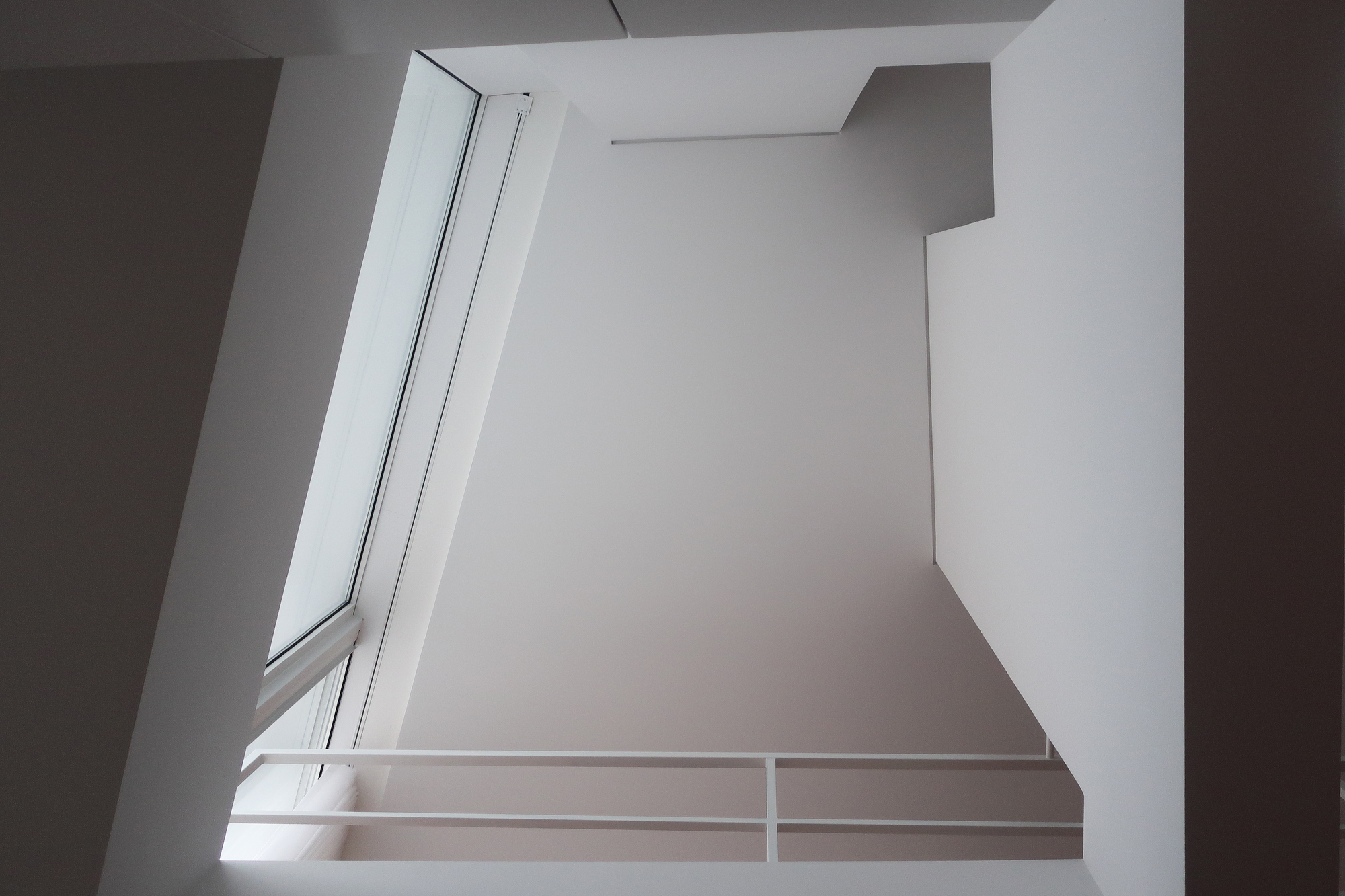 Upward view of a double-height void with angled clerestory windows and a white railing