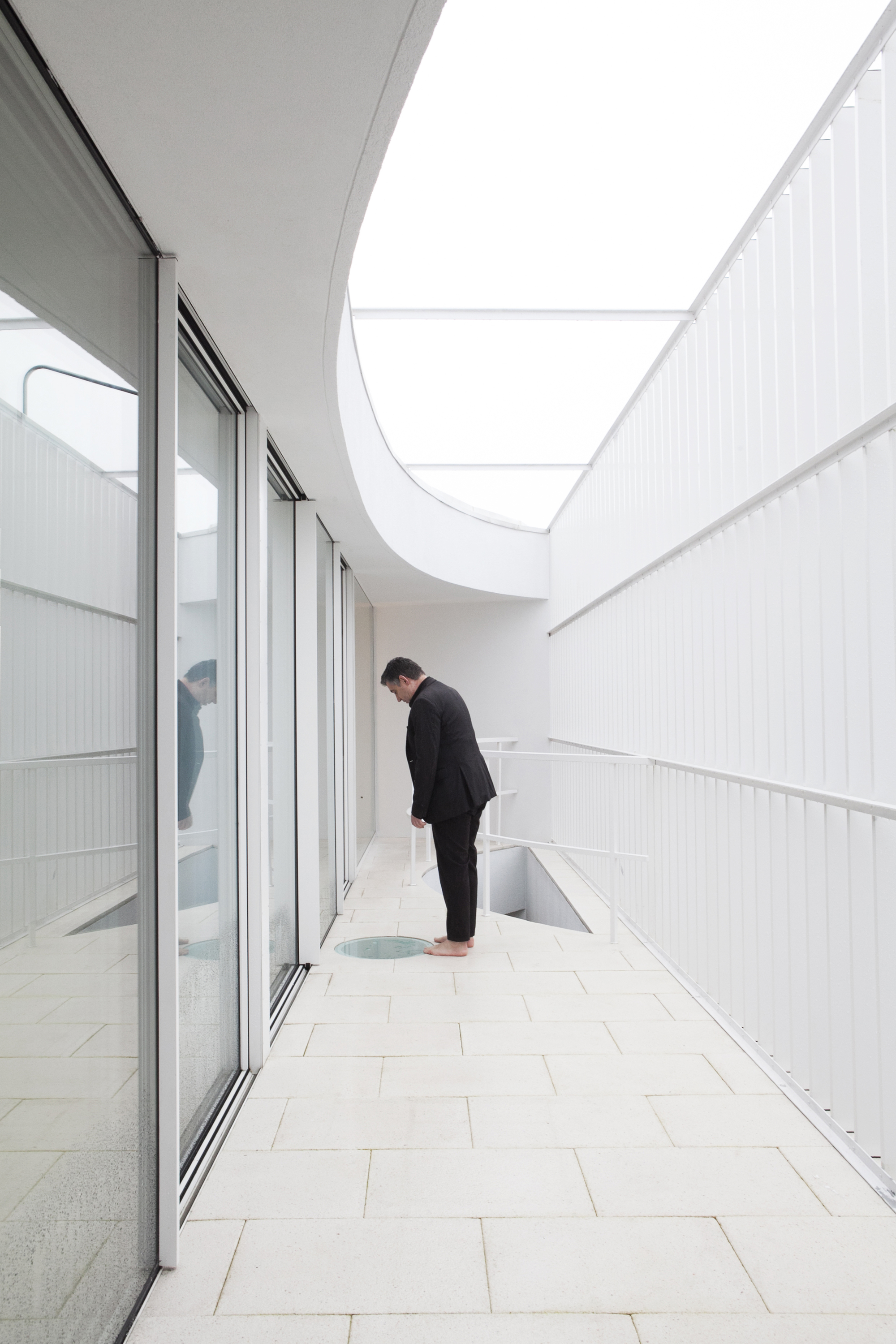 Outdoor terrace with white tile flooring and a person beside a curved skylight opening