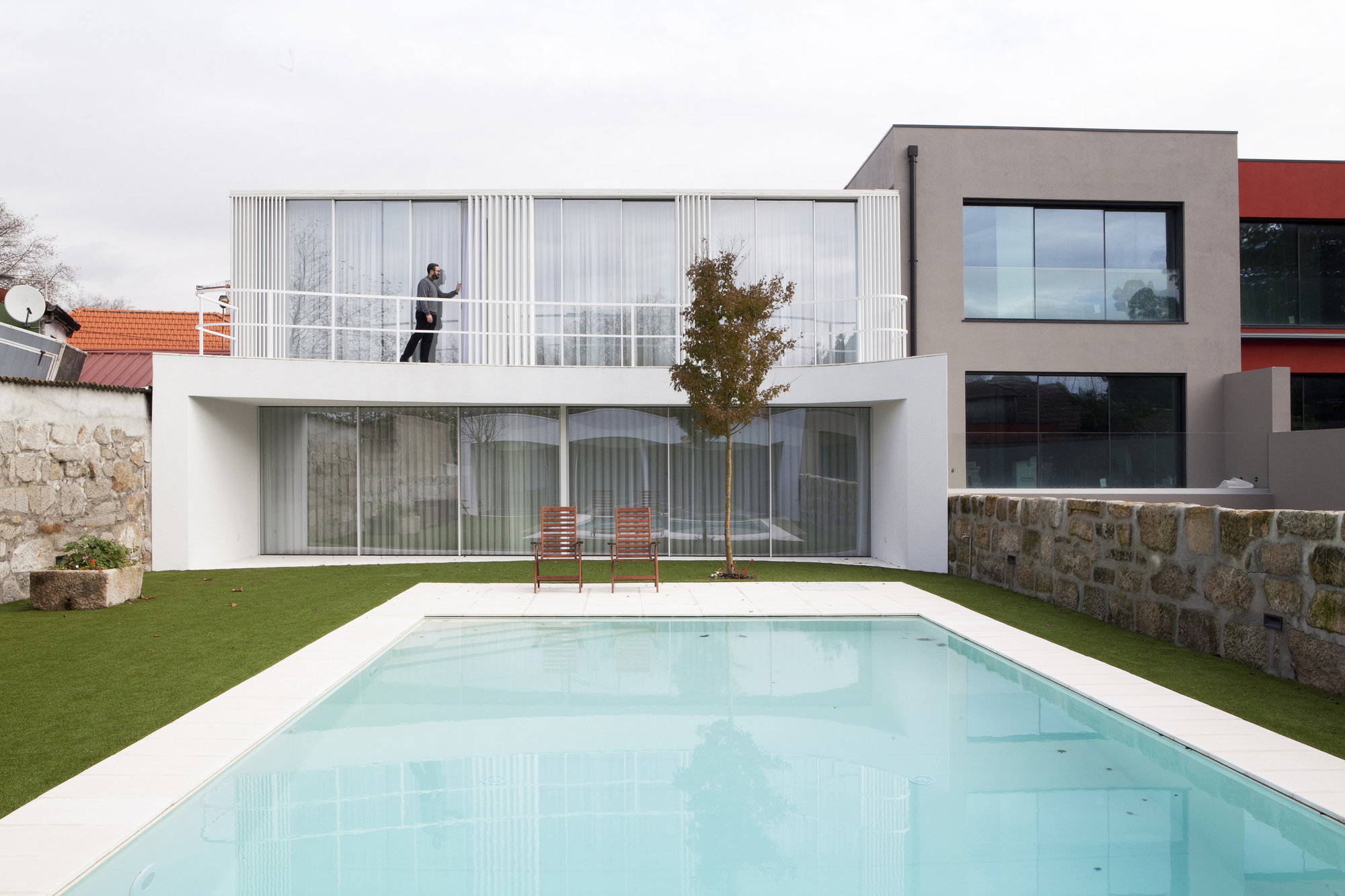 Garden facade with pool, vertical aluminum louvers and stacked volumes with a figure on the upper balcony