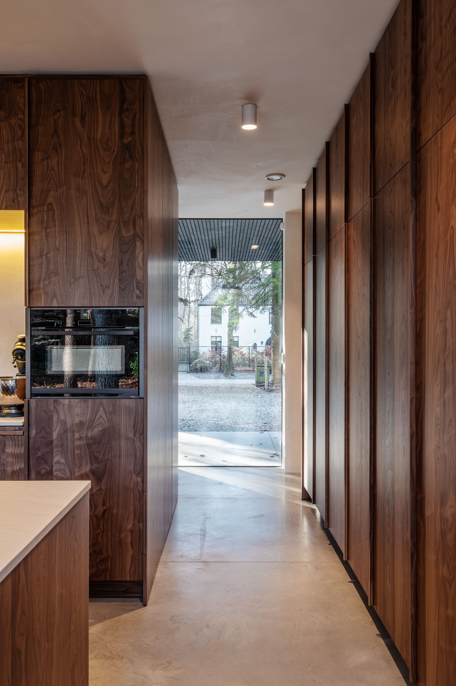 Corridor with walnut millwork walls and polished concrete floor leading to a glass door