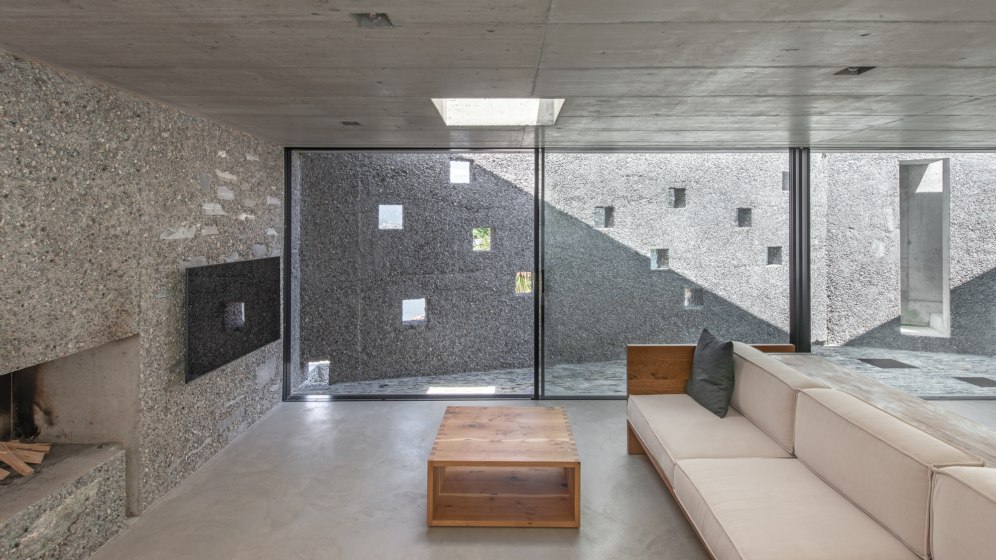 Living room with concrete ceiling and floor-to-ceiling glazing framing an interior courtyard with exposed concrete walls