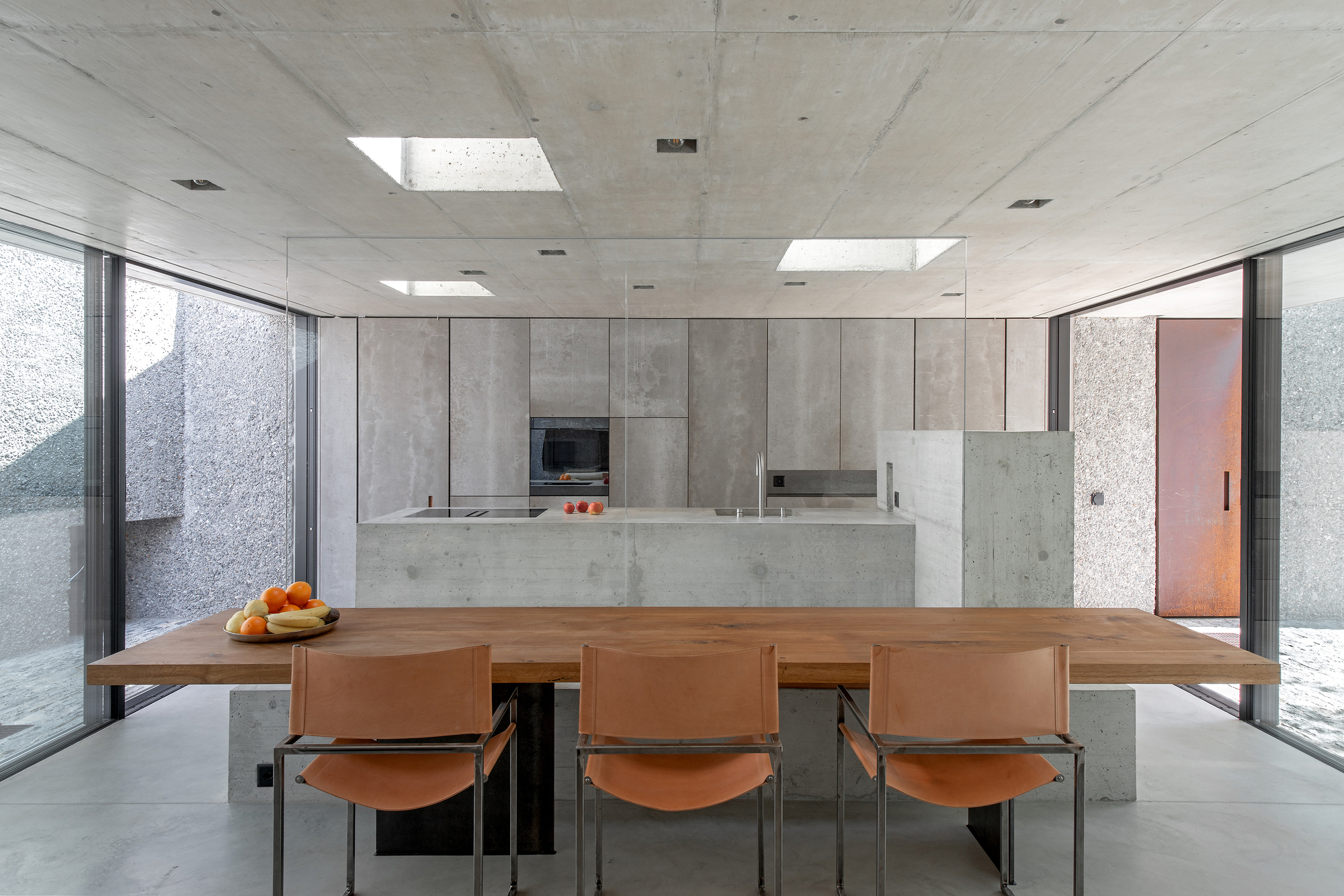 Open kitchen and dining area with concrete island, timber table and skylights above polished concrete floor