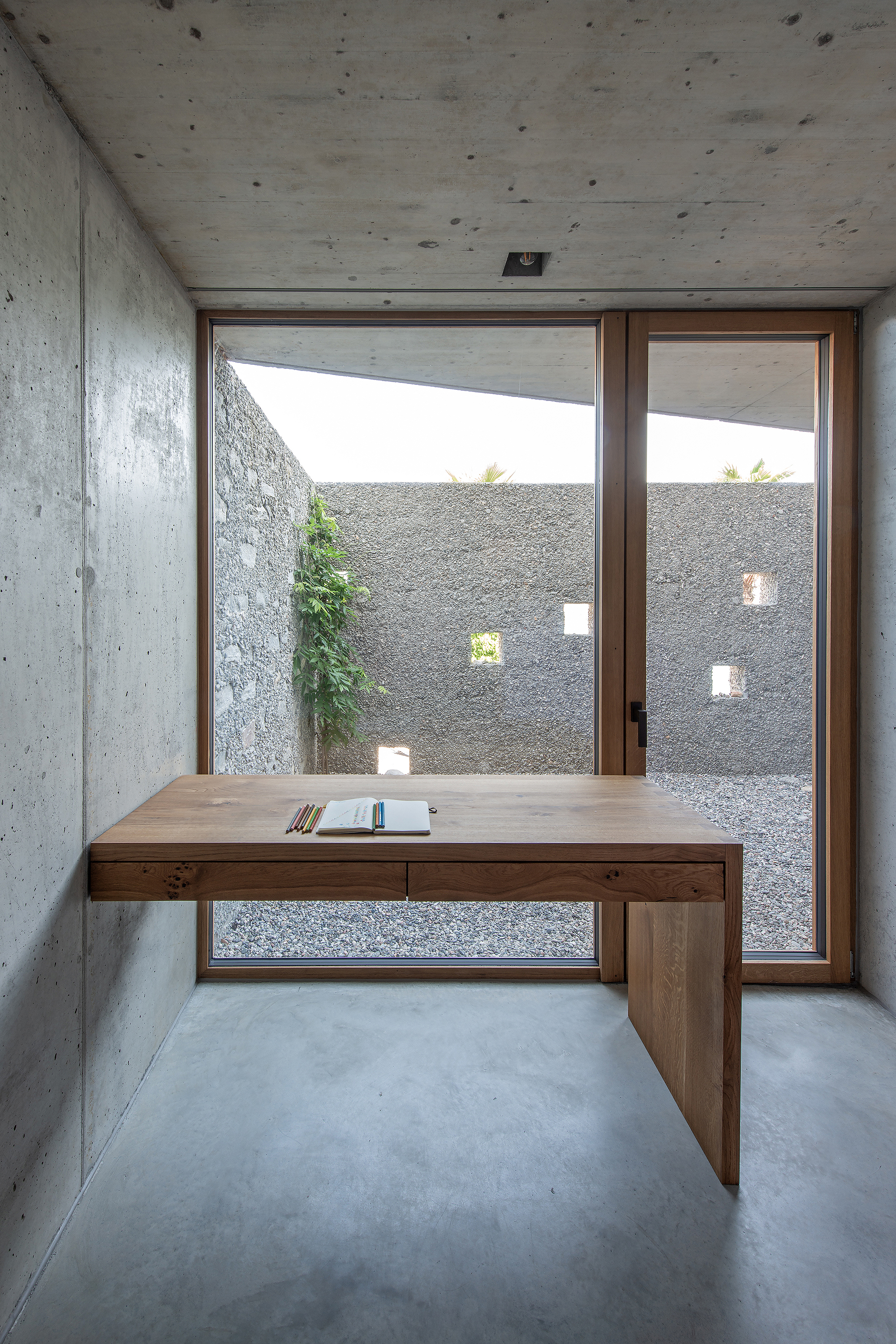 Timber desk positioned in front of glazed doors overlooking a planted courtyard with aggregate walls