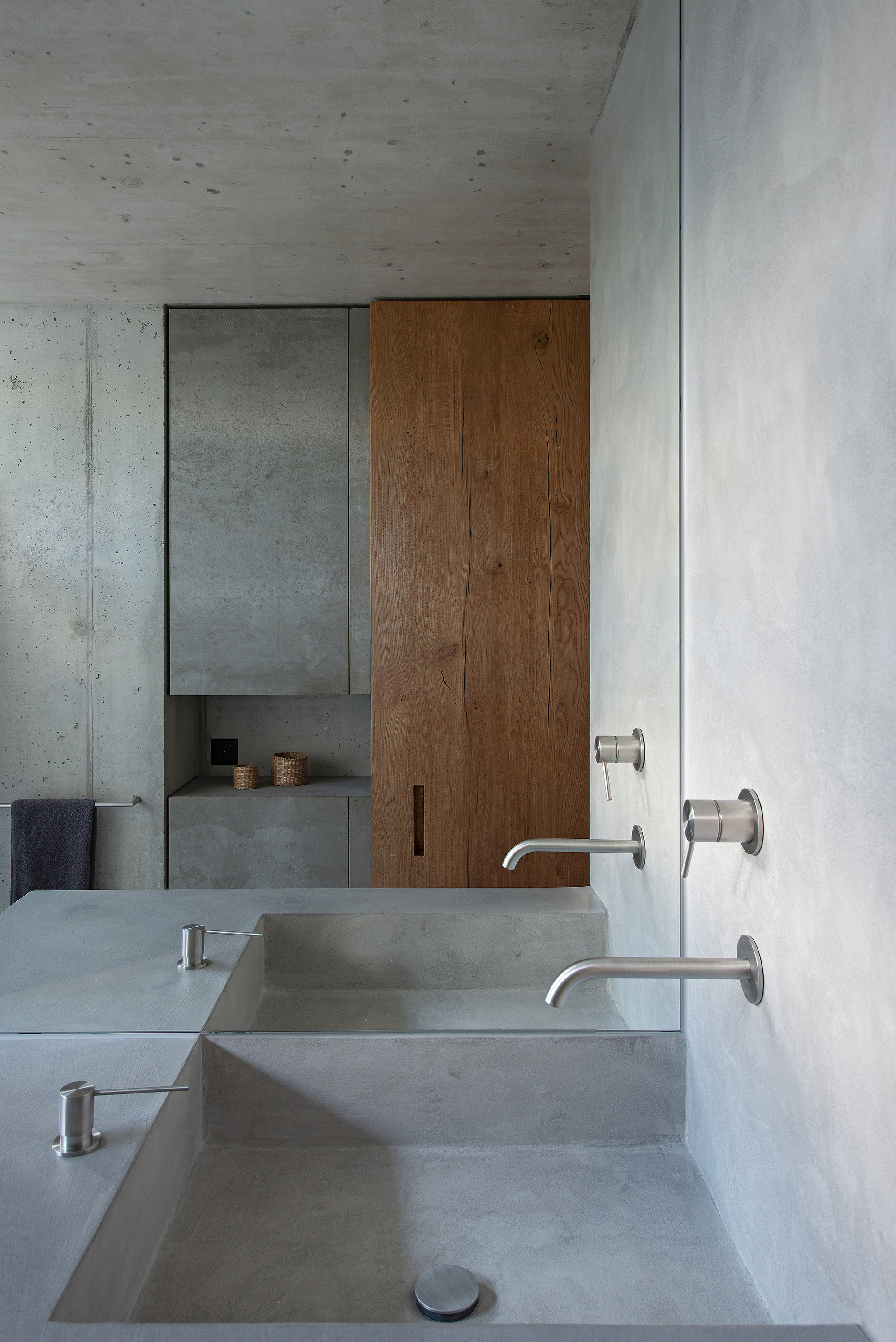 Concrete bathroom vanity with integrated sinks and wall-mounted faucets beneath wood paneling