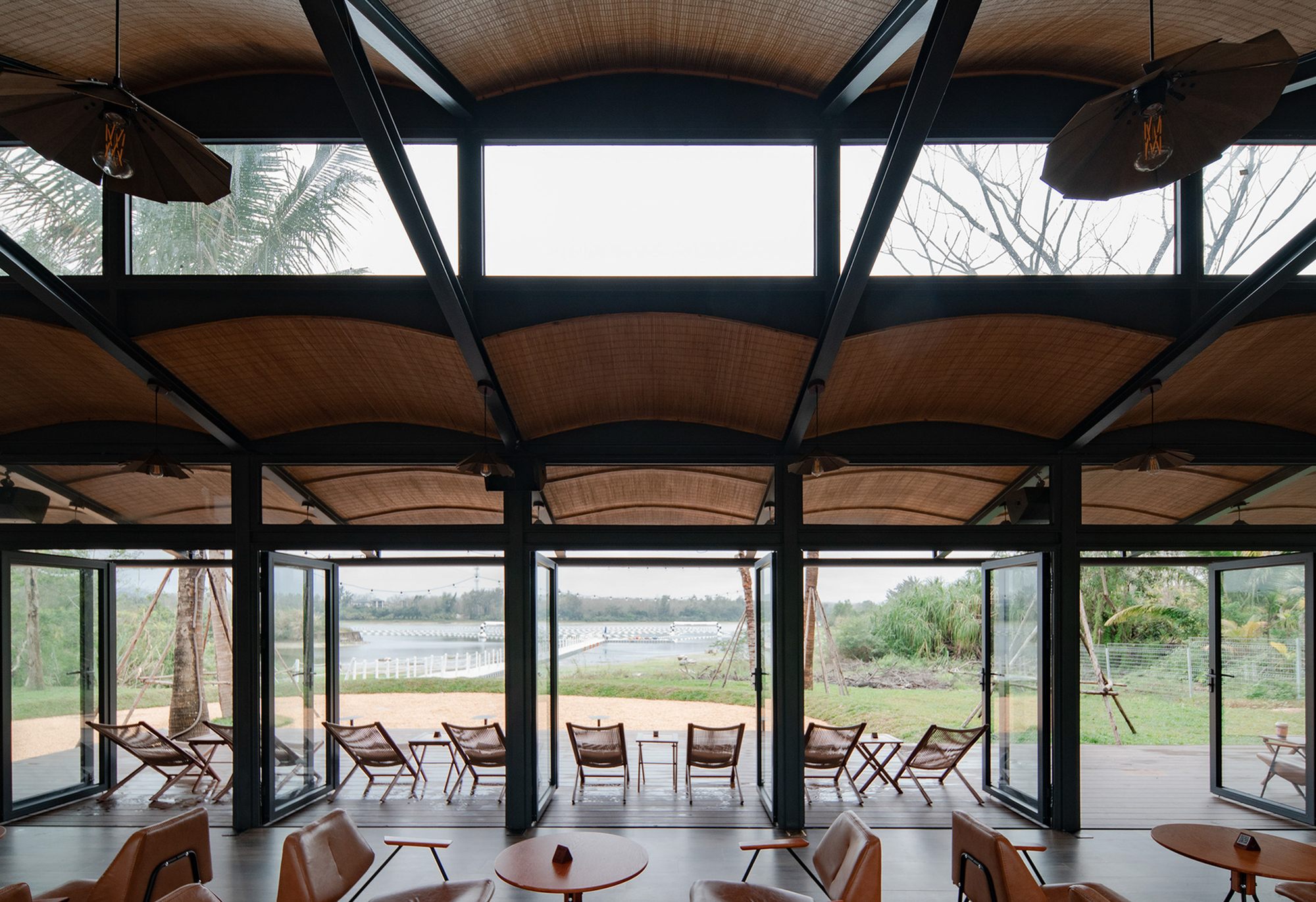 Interior view showing arched woven ceiling panels suspended between black steel trusses with clerestory windows above