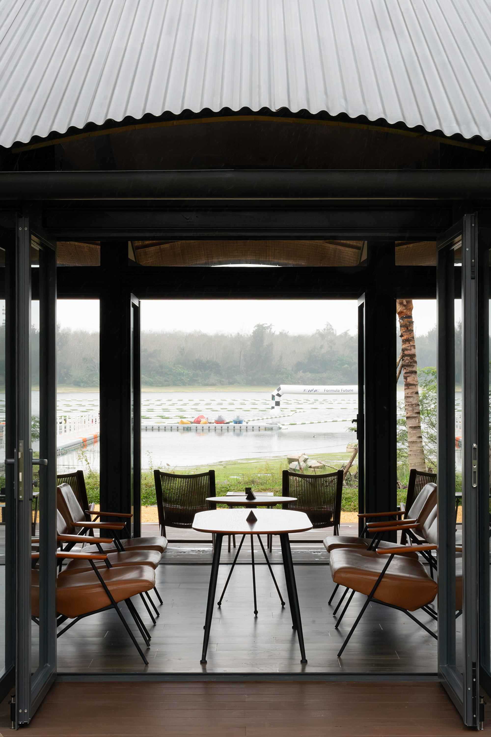 Framed view through the pavilion opening toward the misty lake with dining furniture in the foreground