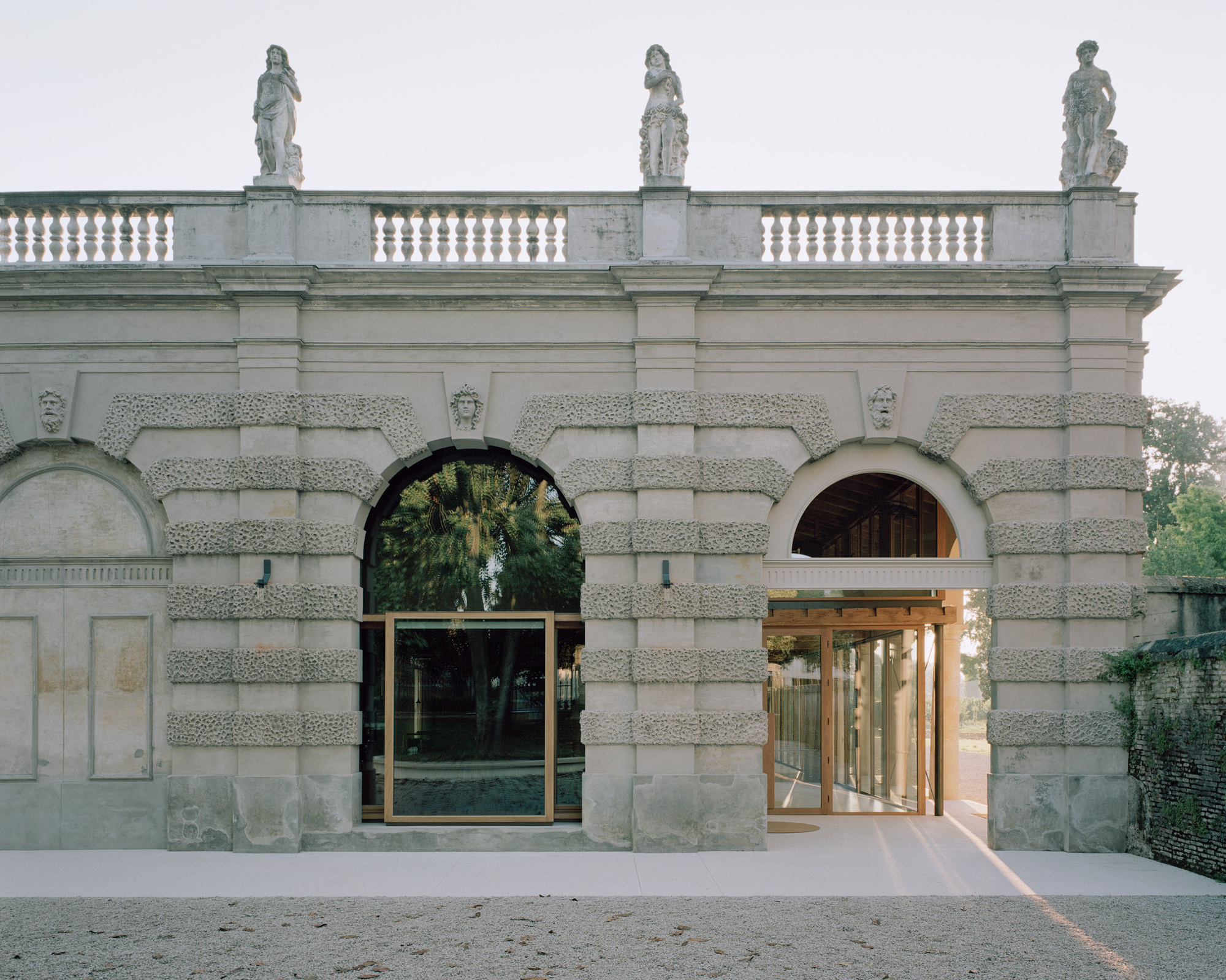 Rusticated stone gateway with arched openings flanked by new bronze-framed glass doors at dusk