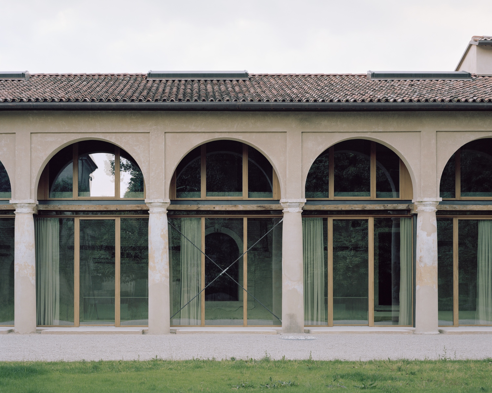 Arcade facade with arched openings and glazed bronze-framed doors beneath a tiled roof
