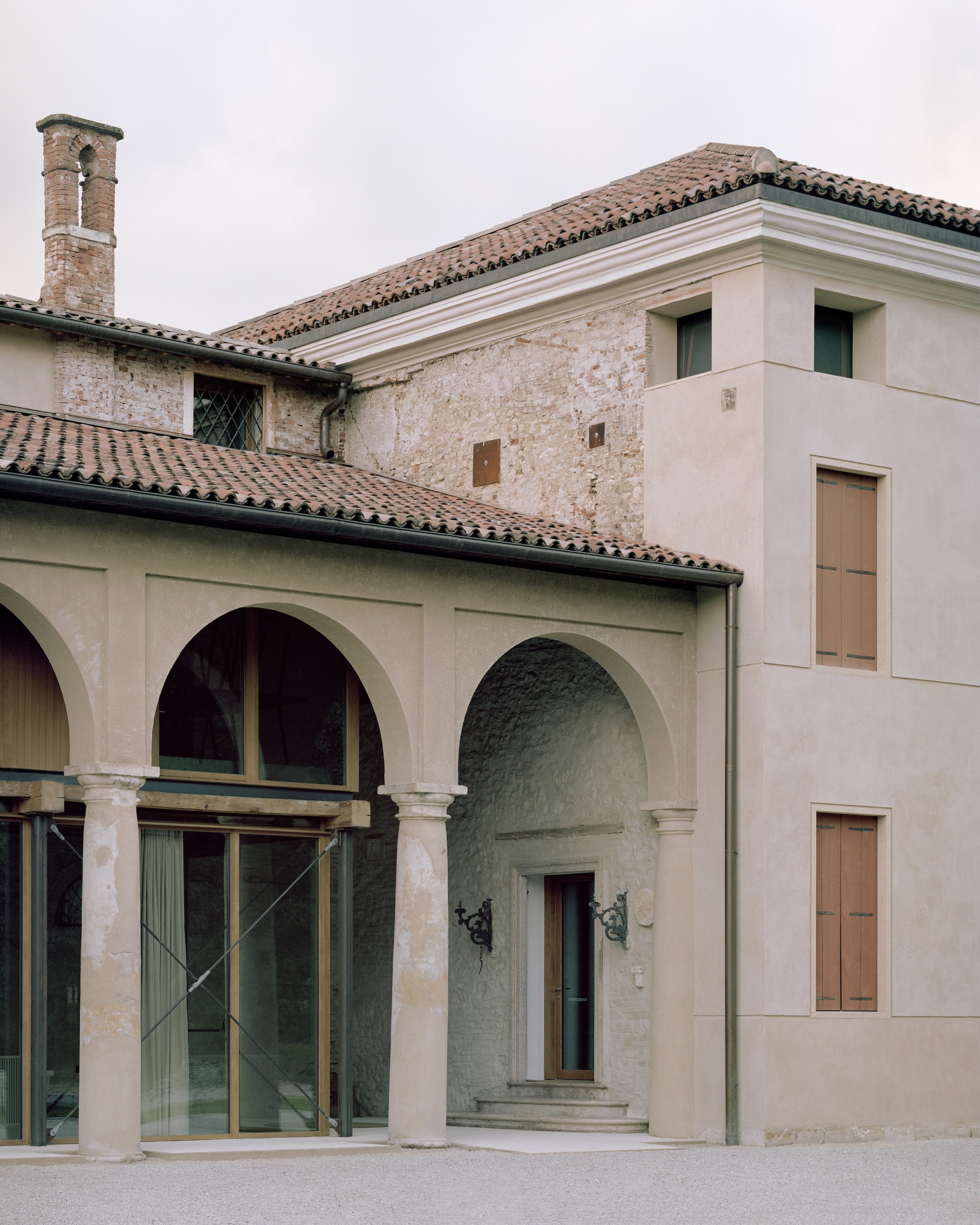 Courtyard view showing the arcade, arched entry portal, and historic brick chimney under overcast sky