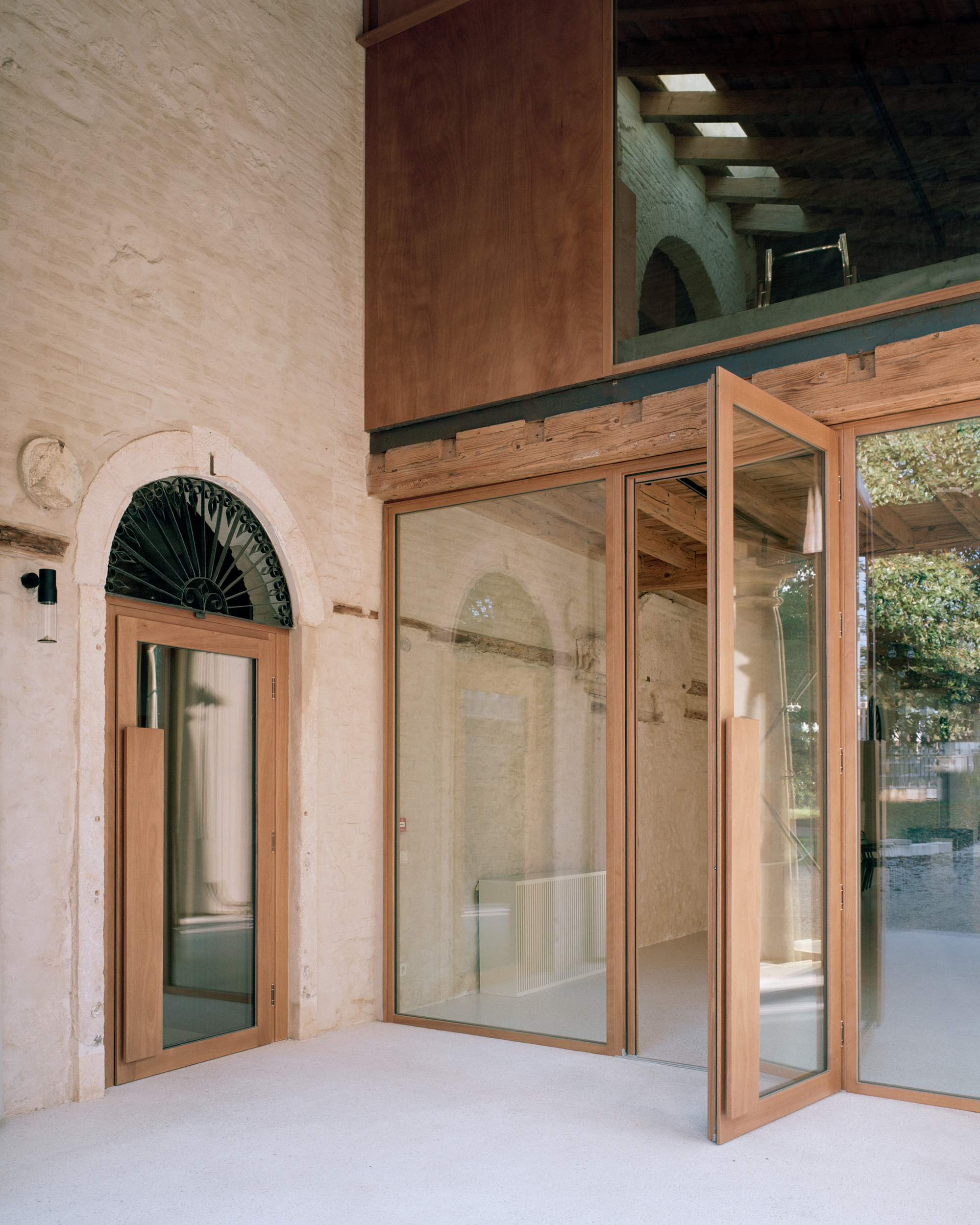 Open timber-framed glass doors with arched transom window and exposed beam mezzanine above