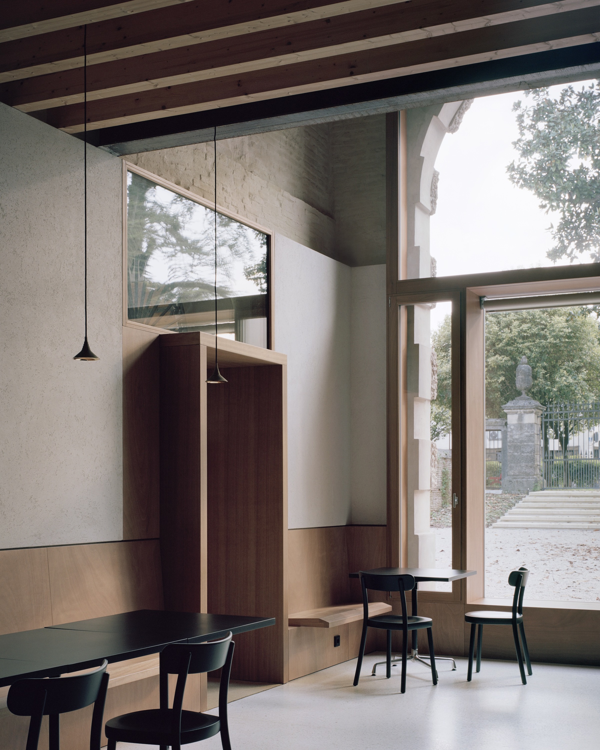 Double-height interior with exposed timber rafters, pendant lights, and black dining chairs by glazed doors
