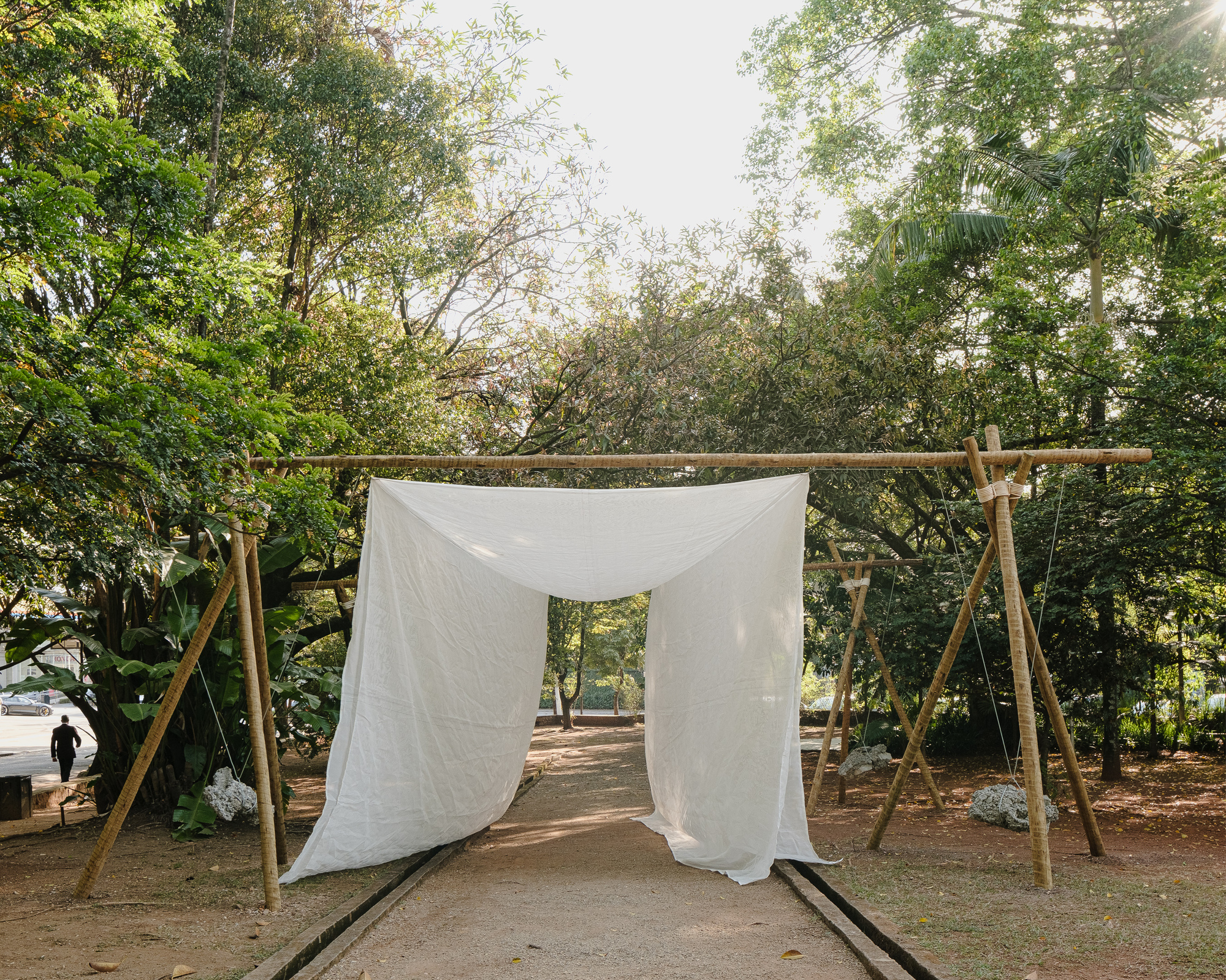 White fabric canopy draped on bamboo frame creating a threshold along a graveled path at dusk