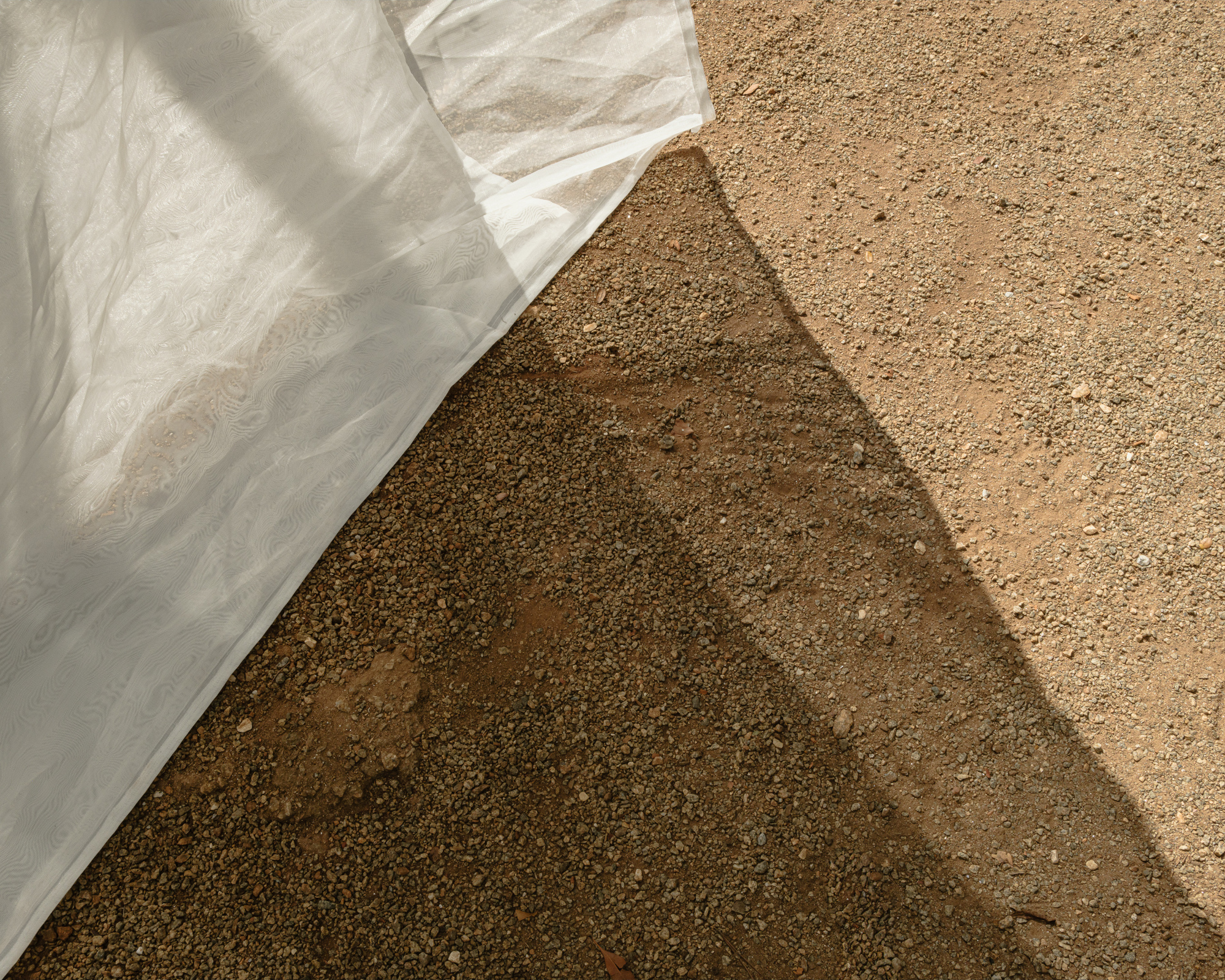 White fabric draped over a triangular formwork casts shadows onto the textured sand surface below